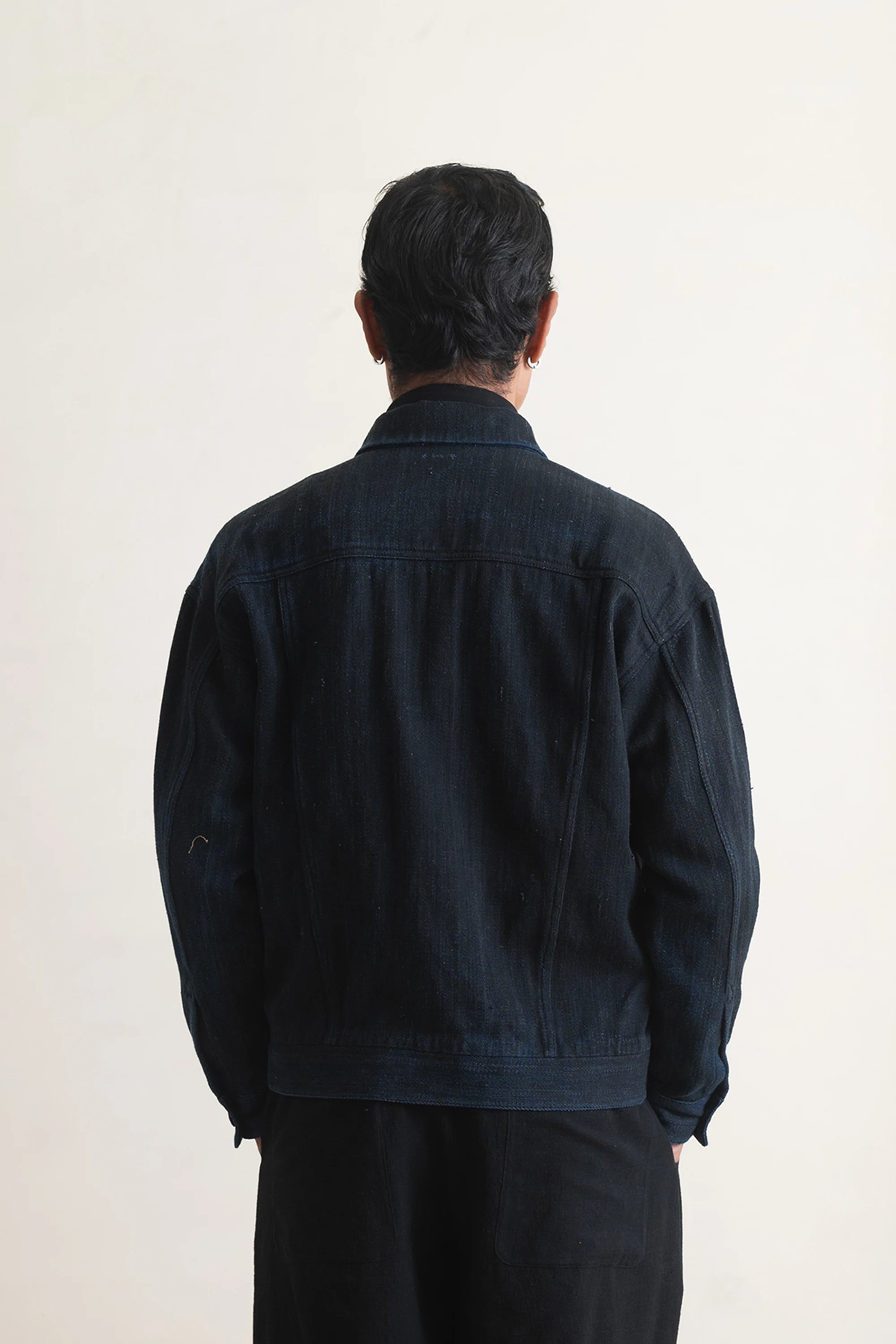 Person wearing a dark jacket and pants against a light grey background