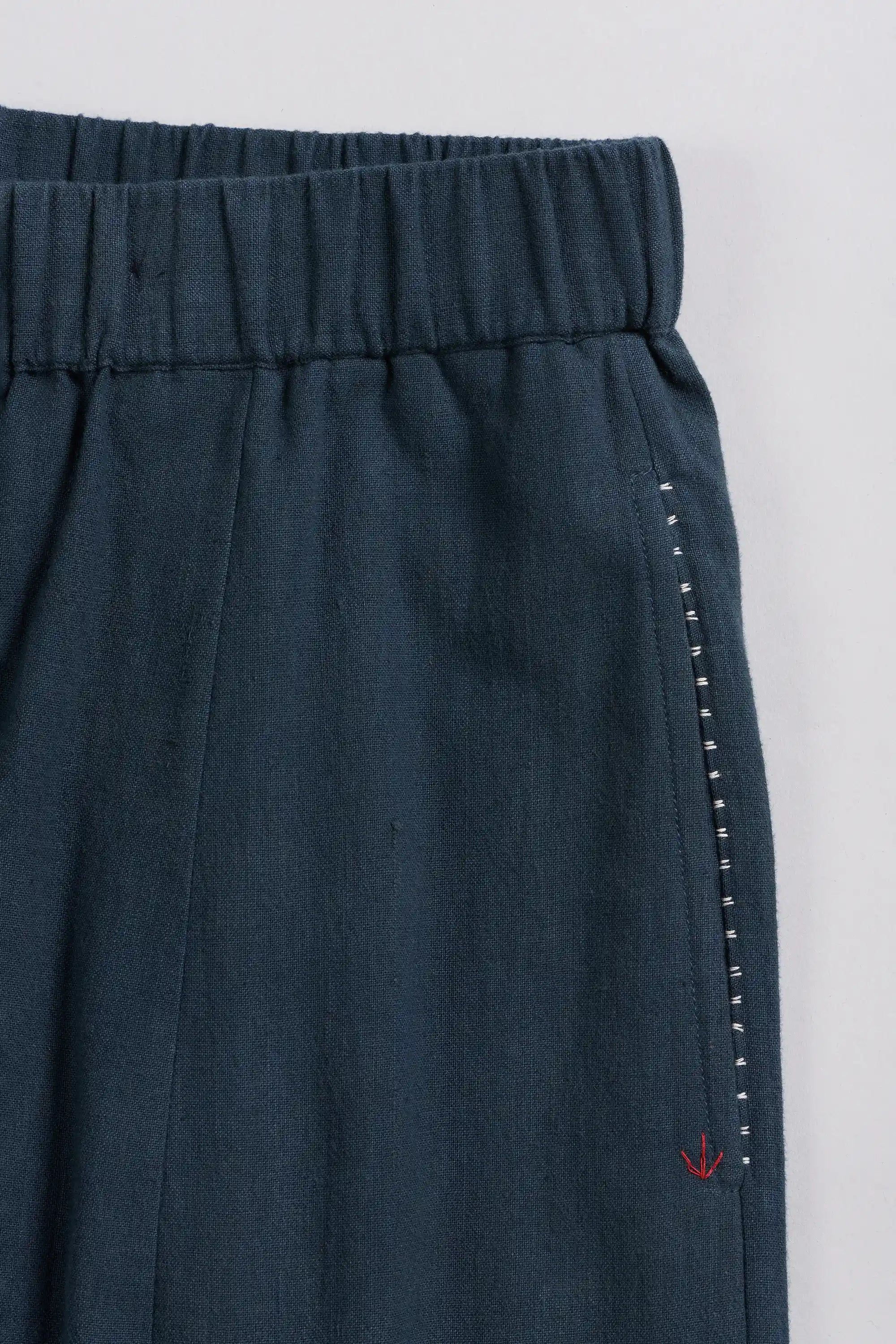 Close-up of black indigo trousers showing the elastic waistband, side seam, and a small red embroidered logo near the hem.