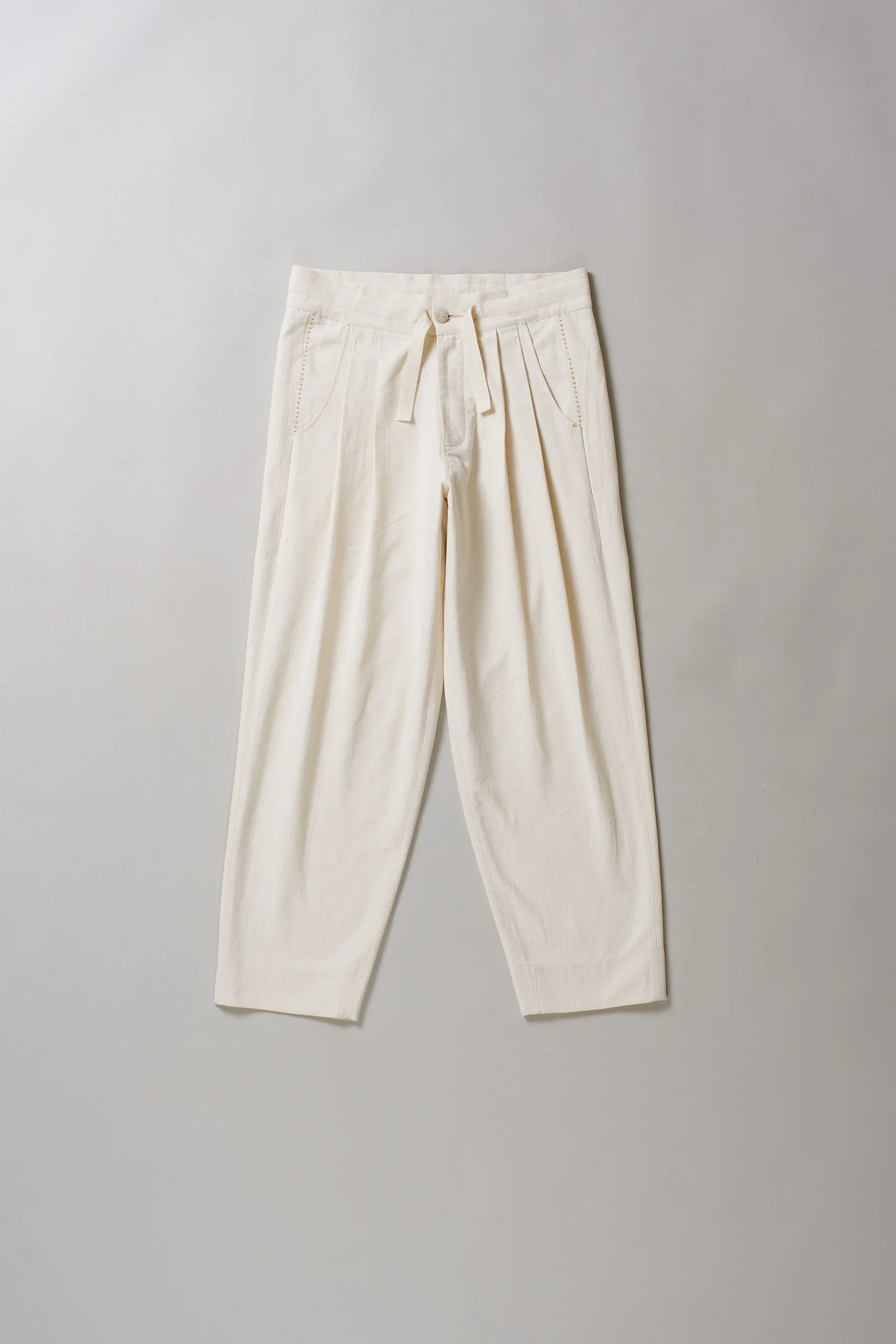 Front image of ecru pants with hand detailing on a grey background