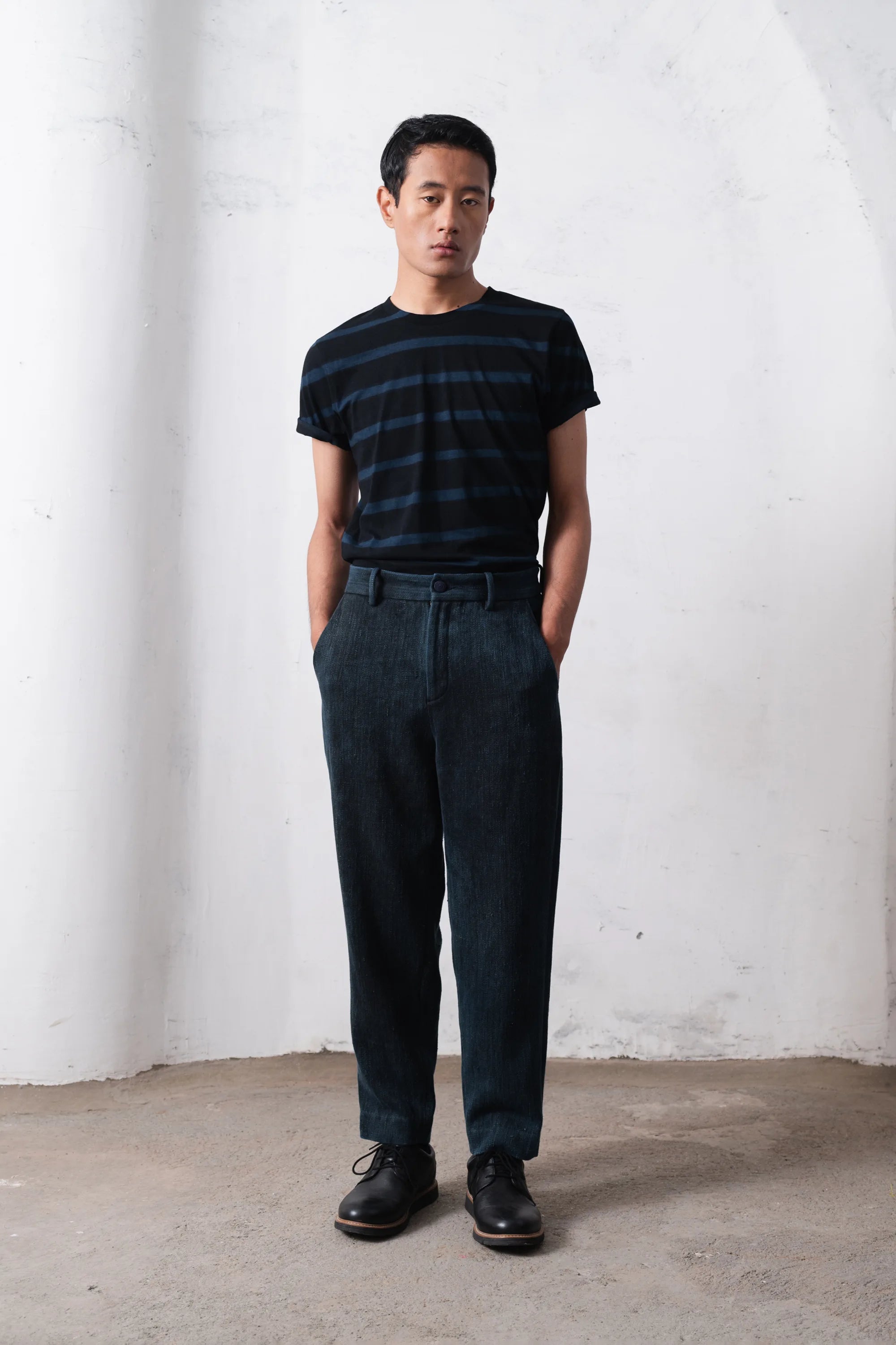 Man wearing a black and blue striped shirt and midnight indigo against a light grey wall