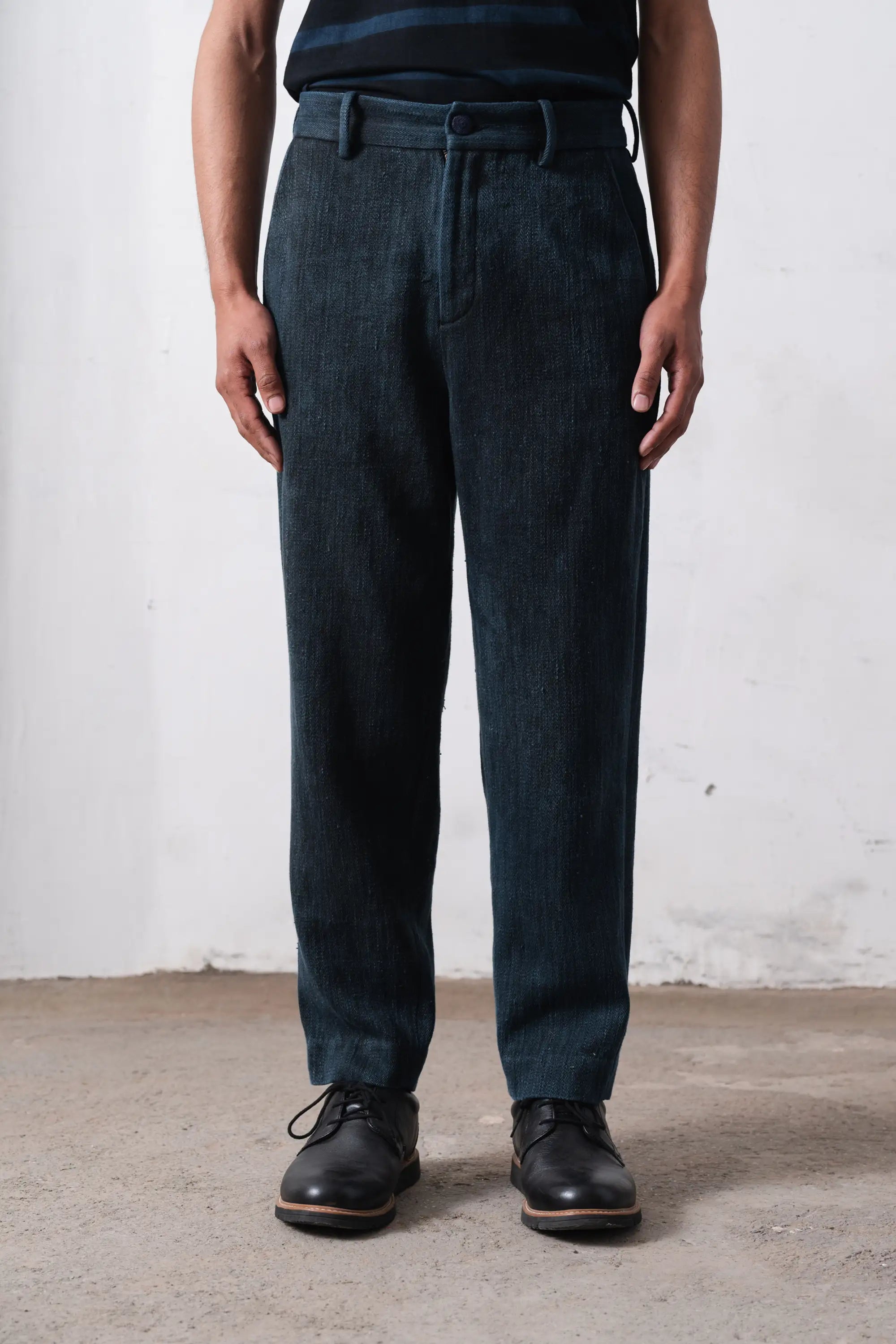 Person wearing midnight indigo pants and black shoes against a light grey wall