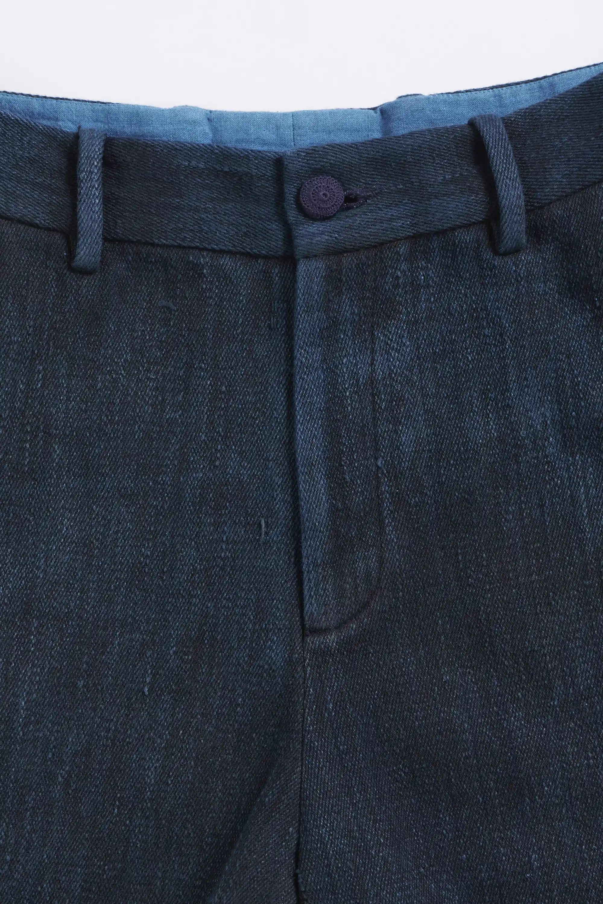 Close-up of midnight indigo pants with a button and belt on a light grey background