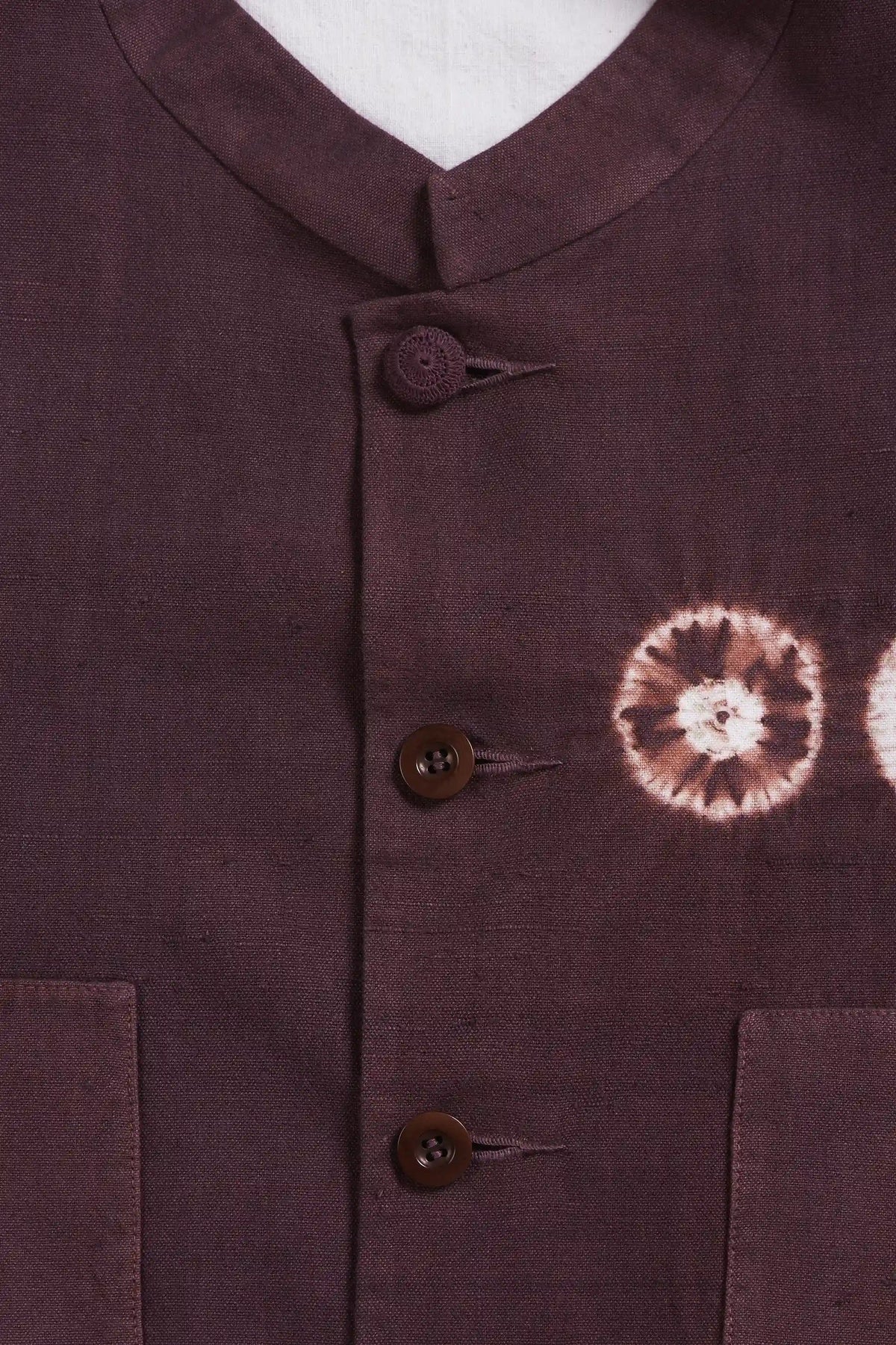 Close-up of a purple vest with three brown buttons and a brown and white tie-dye floral pattern on the chest.