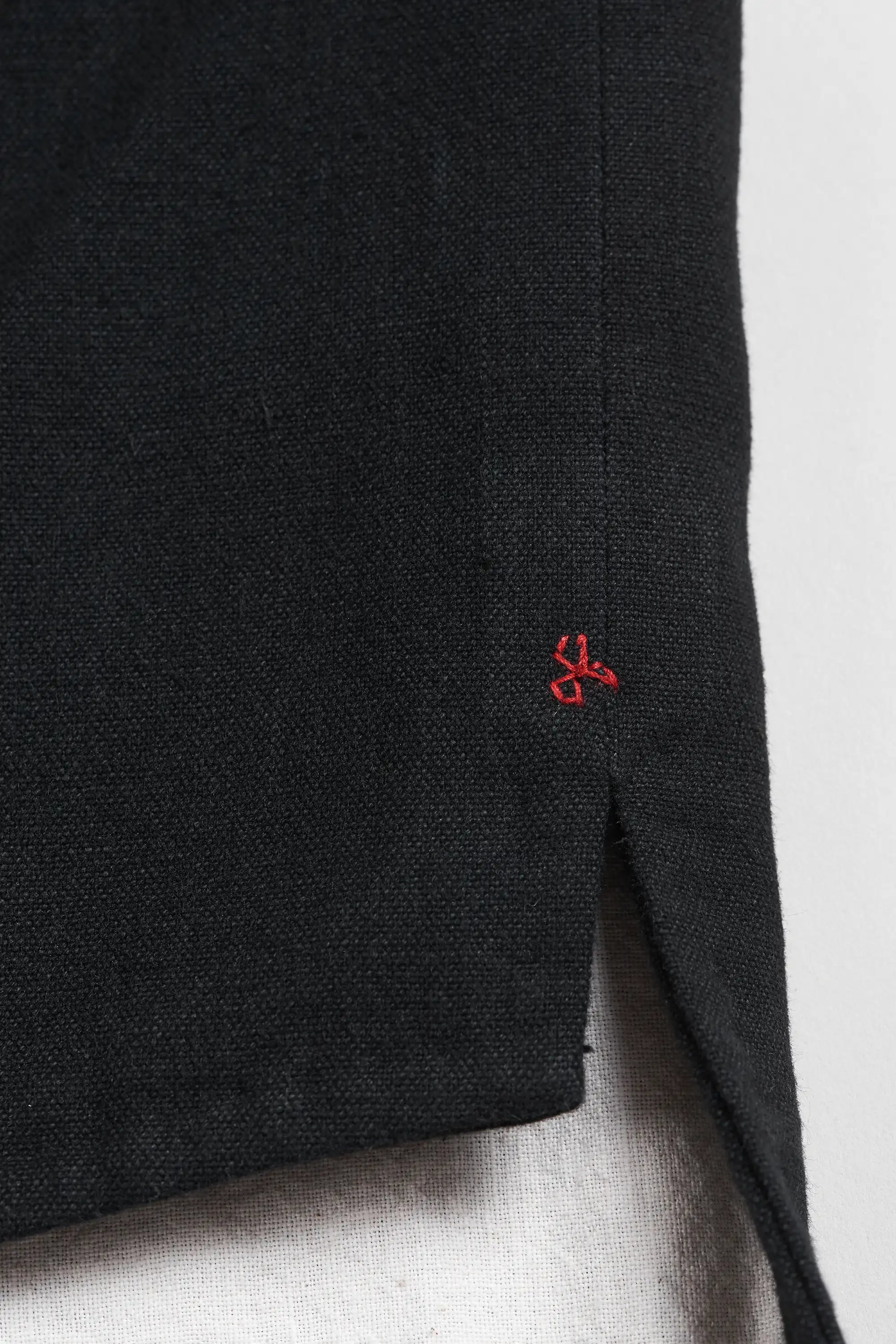 Close-up of a black jacket, showing a small red embroidered logo and a side slit.