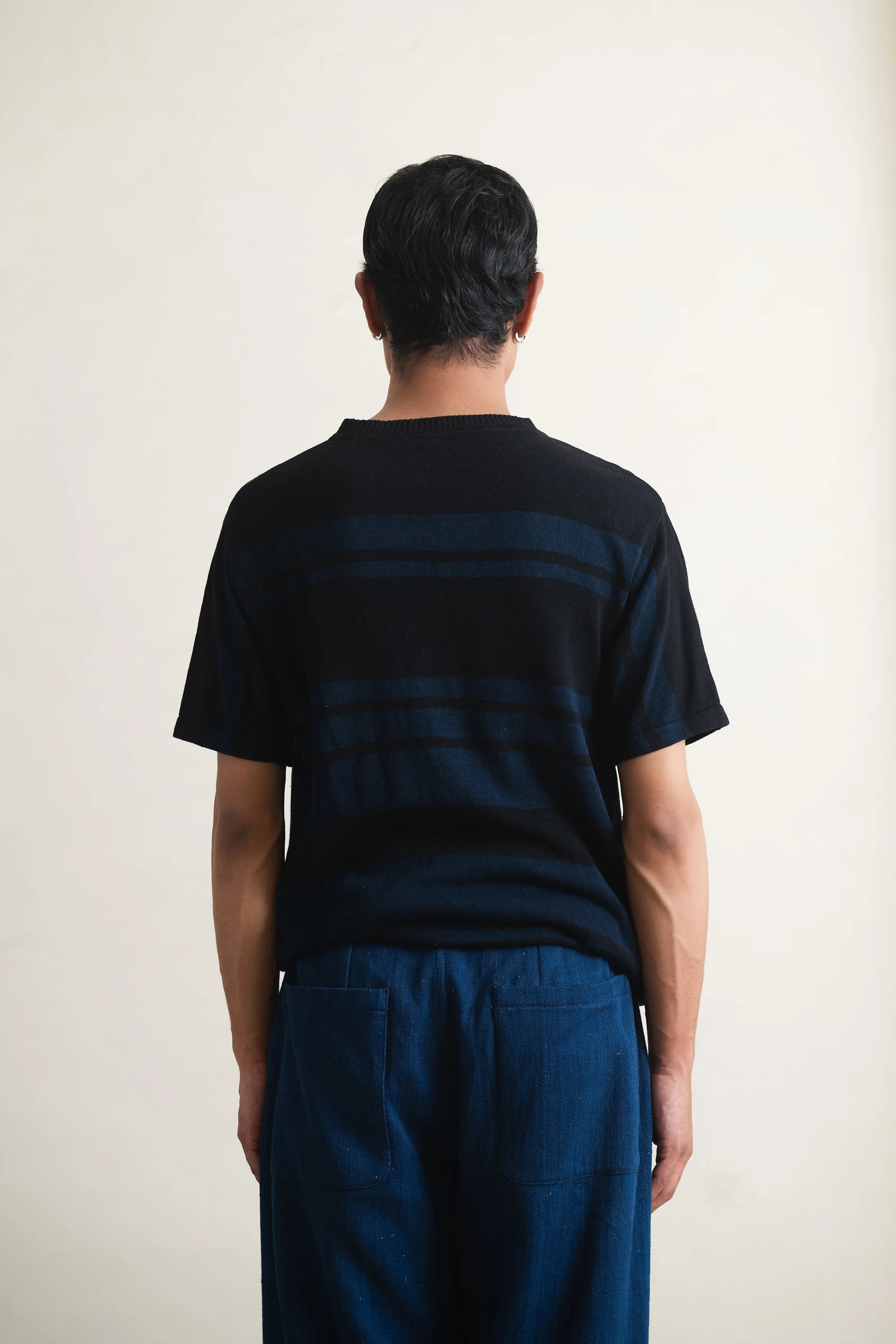 Back shot of a person wearing a black t-shirt and blue pants against a light grey background