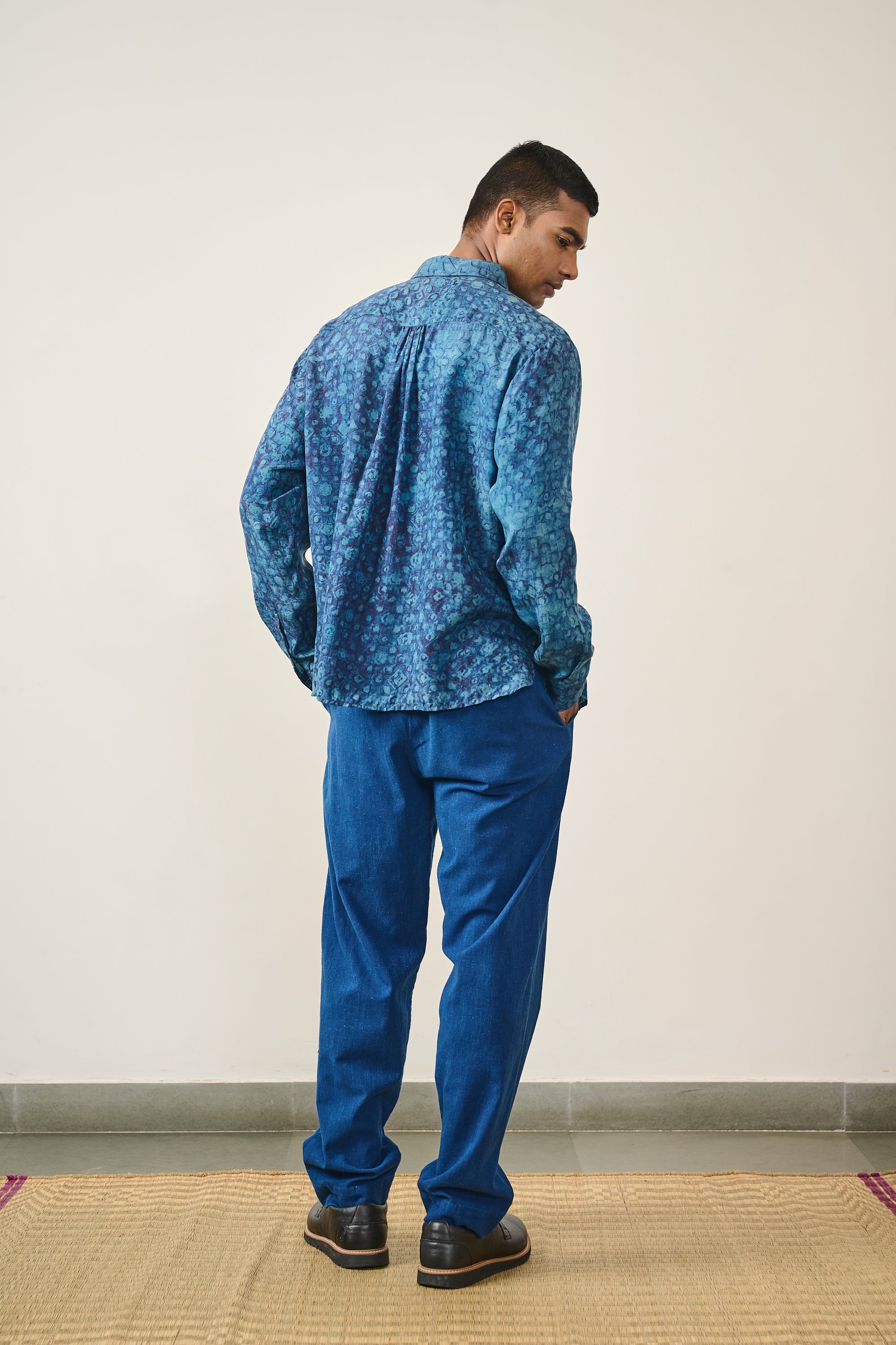 A back shot of a man wearing medium indigo shirt