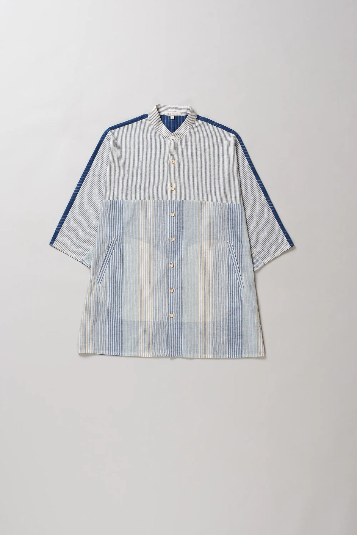 A short-sleeve button-up shirt with a light grey and white striped body, featuring solid blue shoulder yokes and blue stripe accents on the sleeves, laid flat against a light grey background.