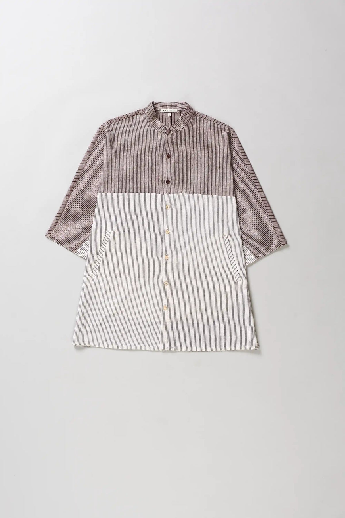 A color-blocked linen shirt with a textured taupe-brown upper half and sleeves, and a light beige lower half, laid flat against a light grey background.
