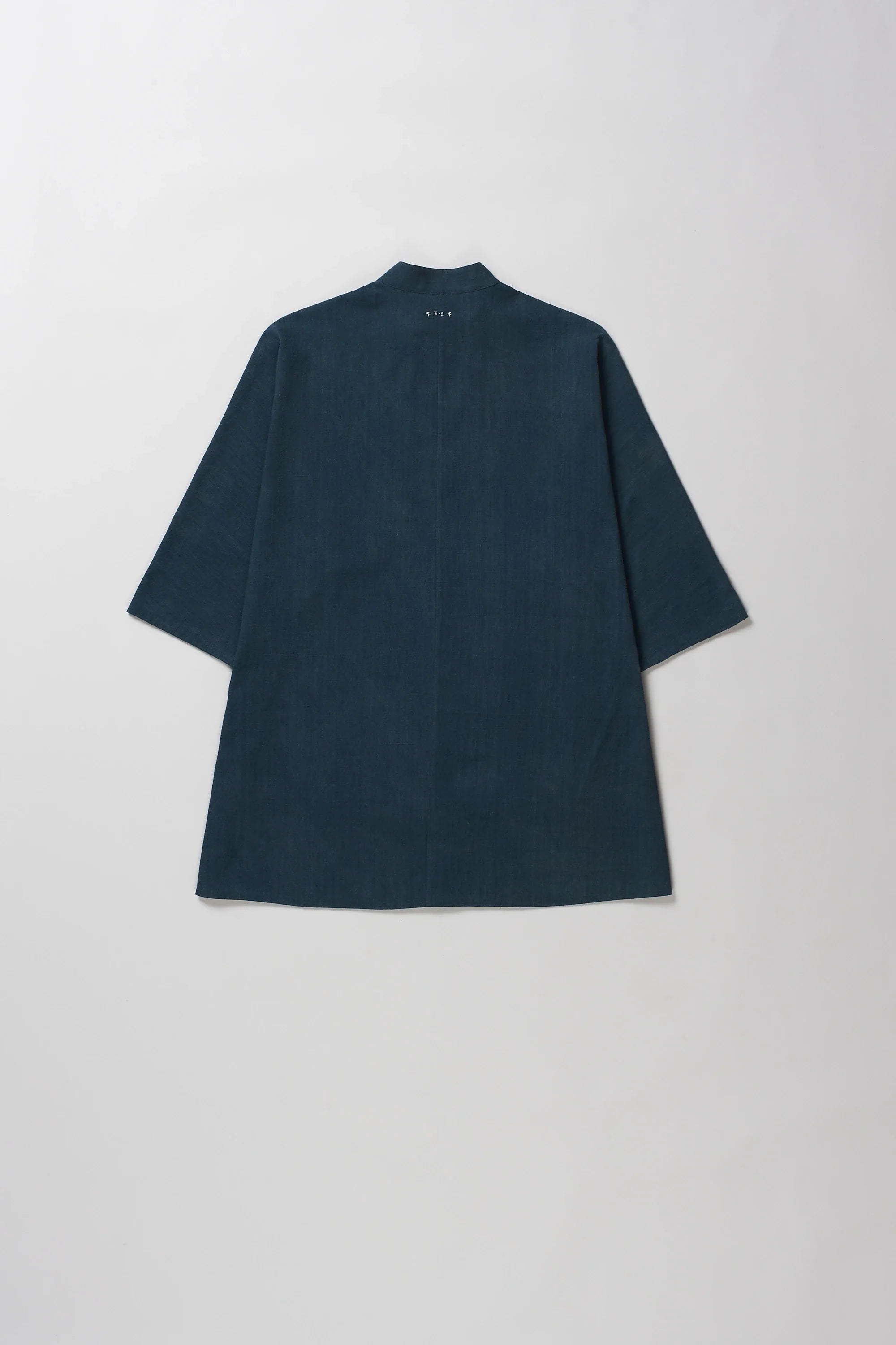 Back shot of half-sleeve button-up shirt with a band collar, laid flat against a light gray background.