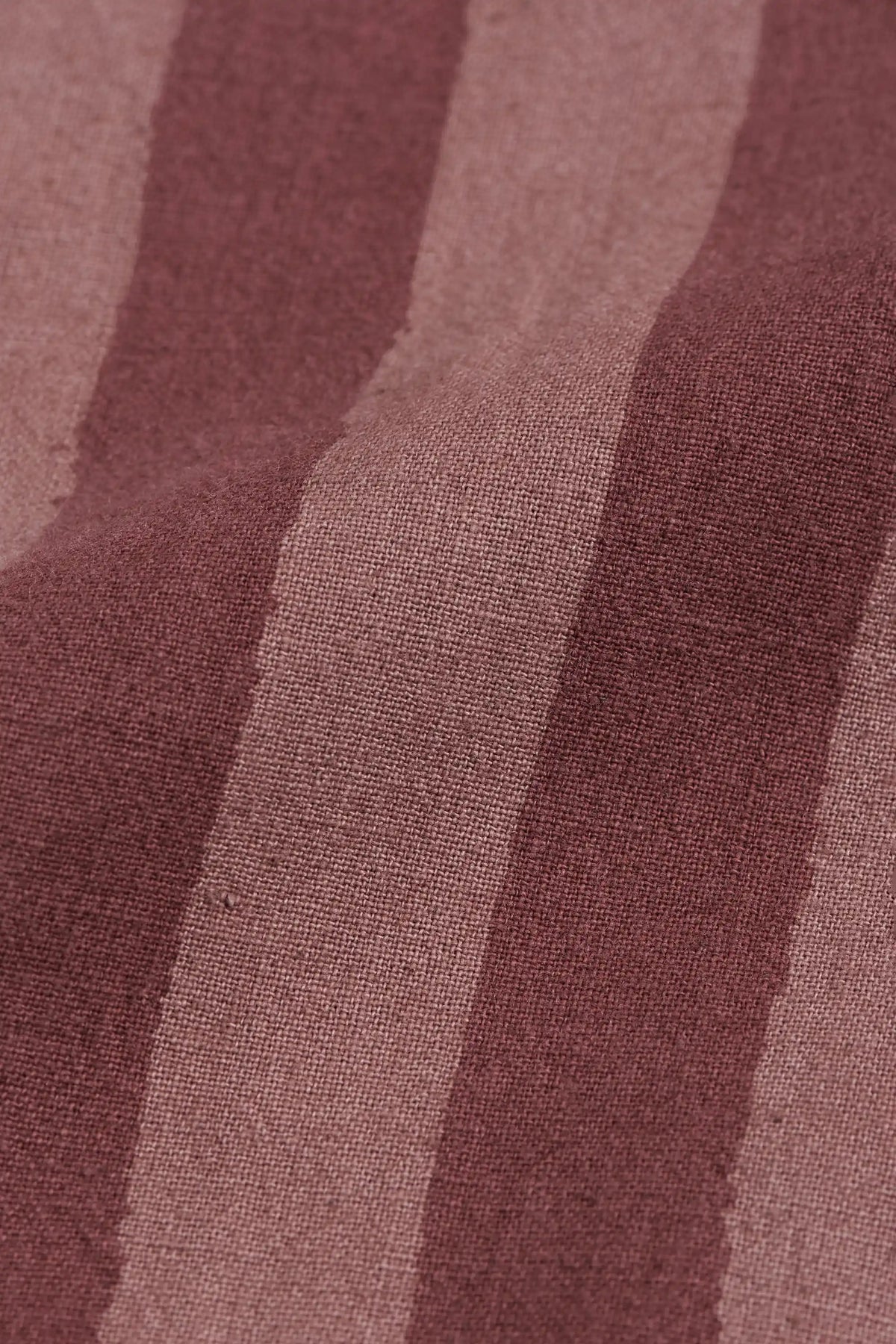 A close-up of a textured fabric with vertical stripes in dusty rose, mauve, and muted brown.