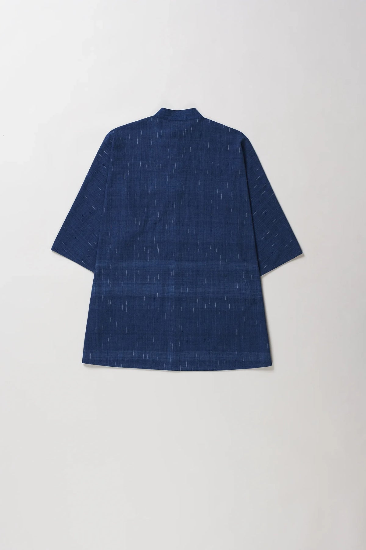 A indigo textured short-sleeve shirt shown from the back, laid flat against a grey background.