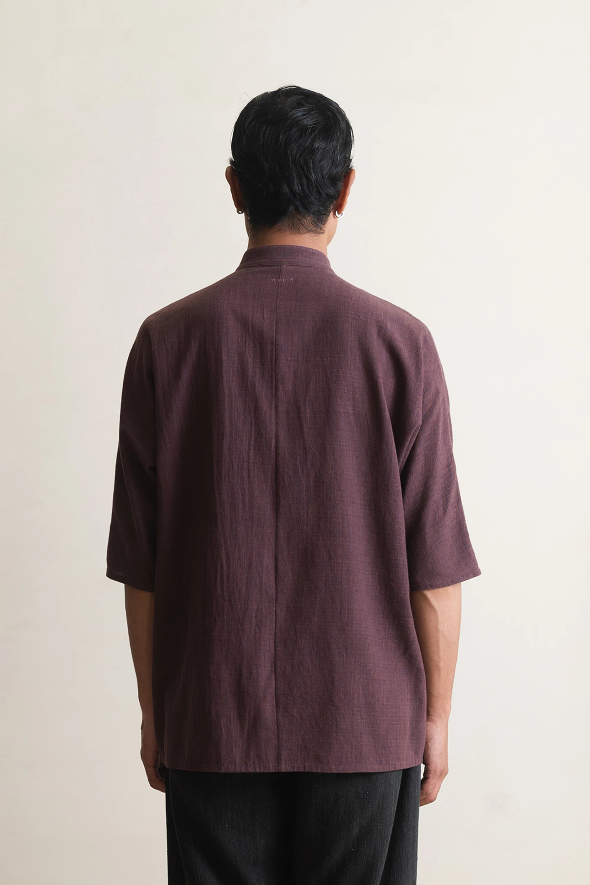 Person wearing a purple red shirt from behind on a light grey background