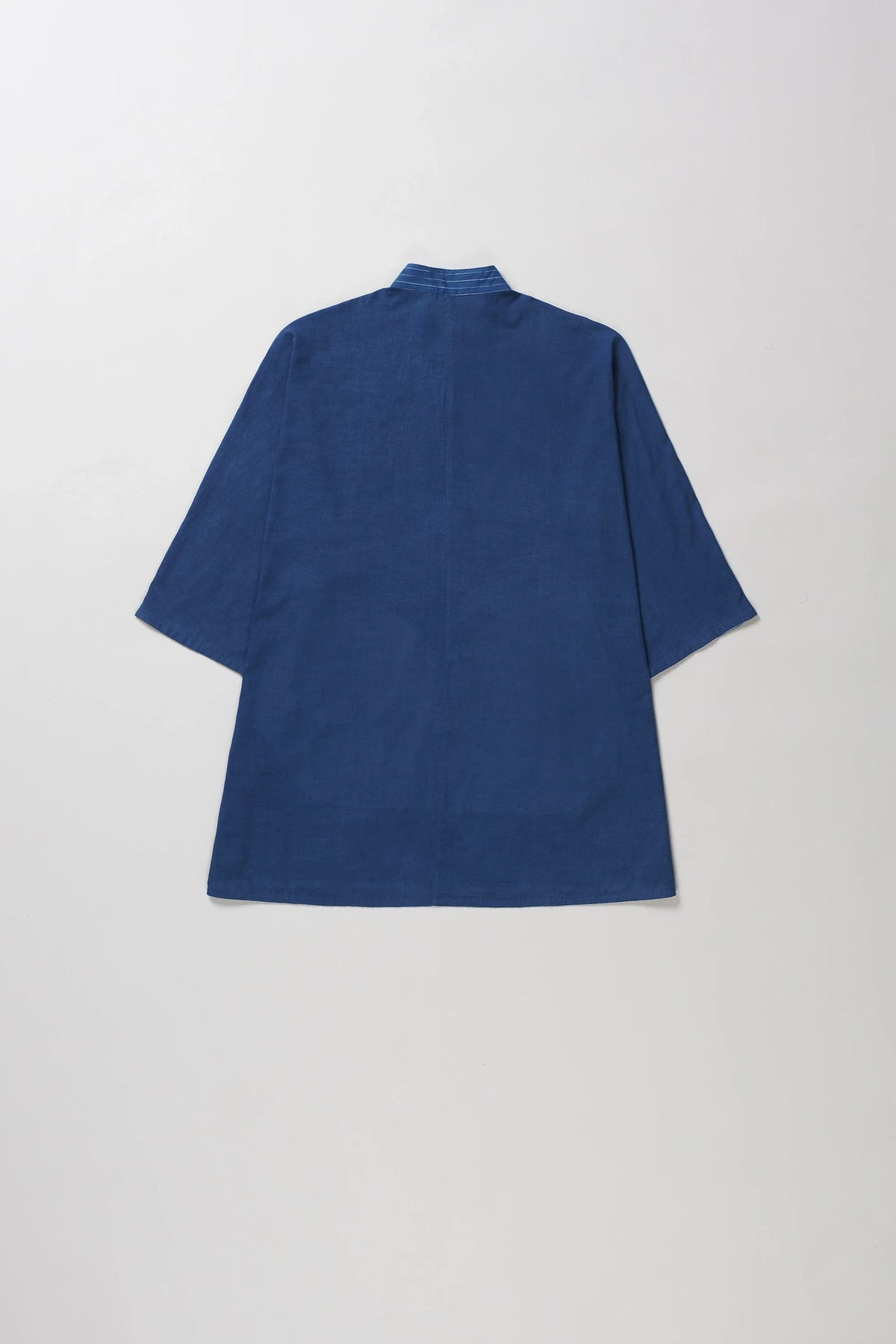 A indigo short-sleeve shirt with a high collar, shown from the back against a light grey background.