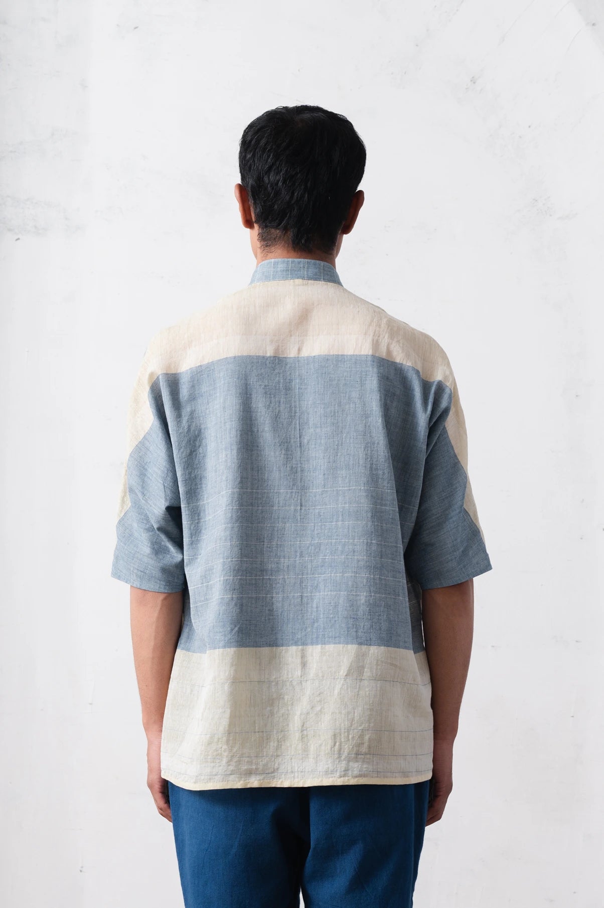 Person wearing a blue and beige checkered shirt with a light grey background