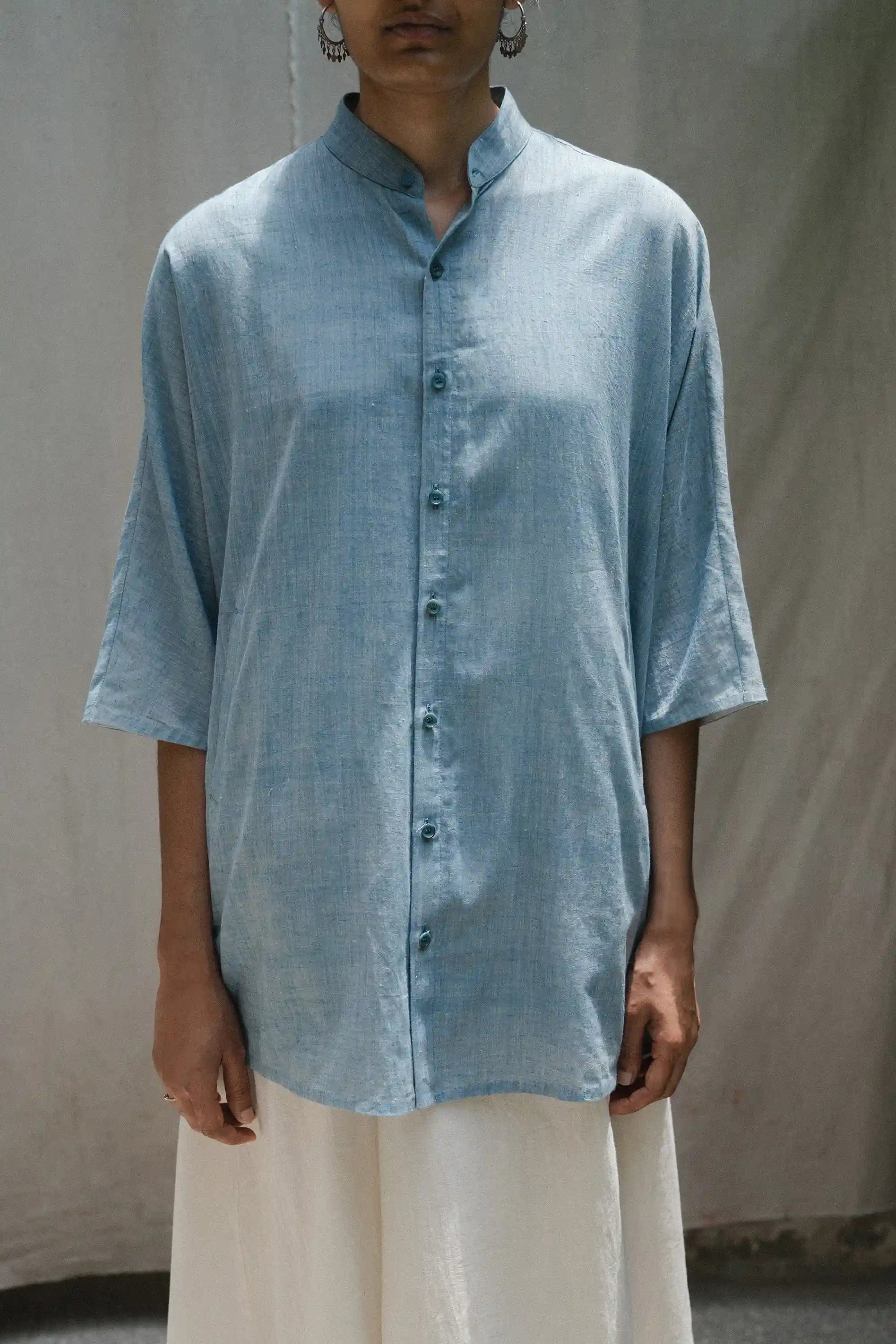 Person wearing a light blue button-up shirt with a grey background