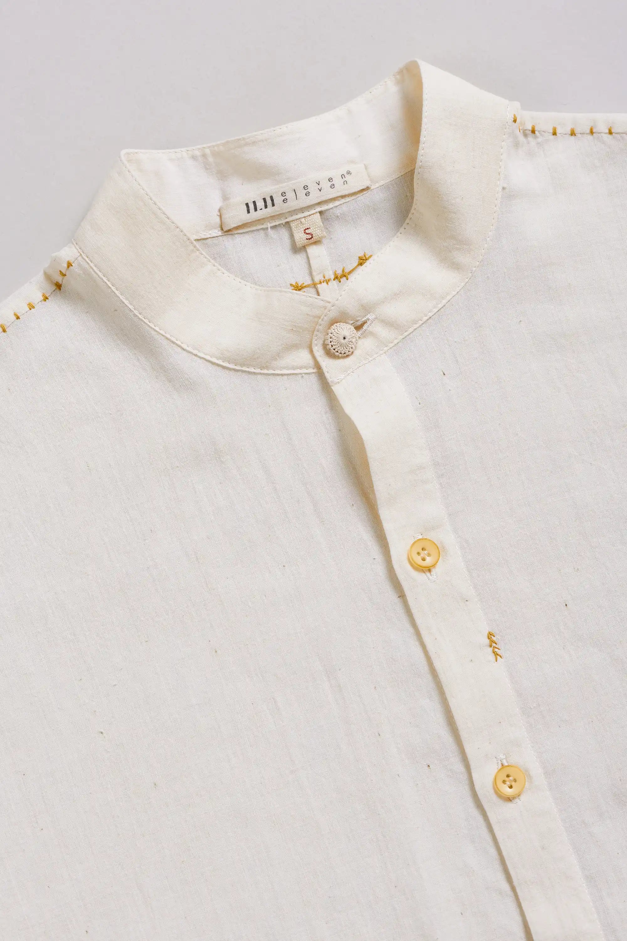 Close-up of a ecru shirt with gold buttons on a light grey background