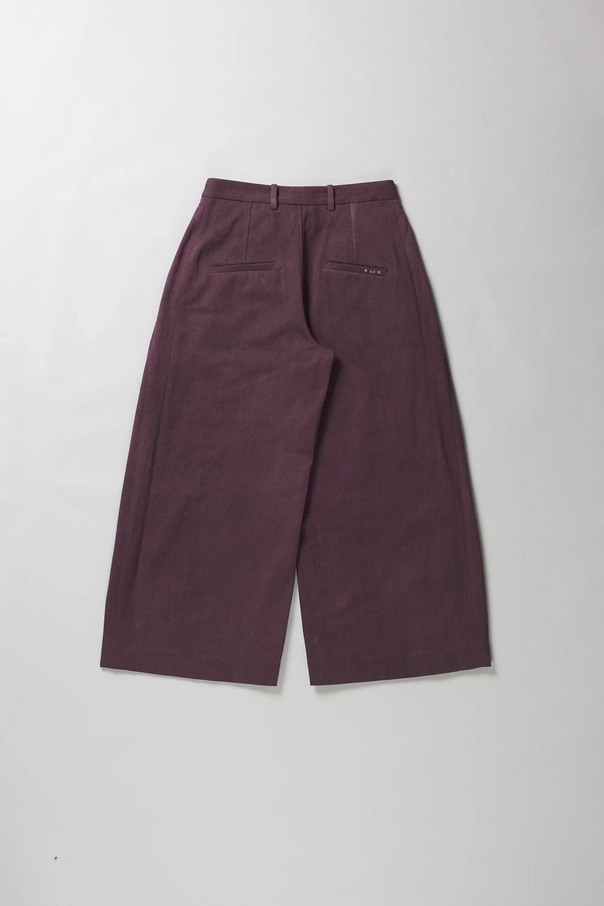 A pair of wide-leg cropped trousers in a muted plum purple color, shown from the back on a grey background.