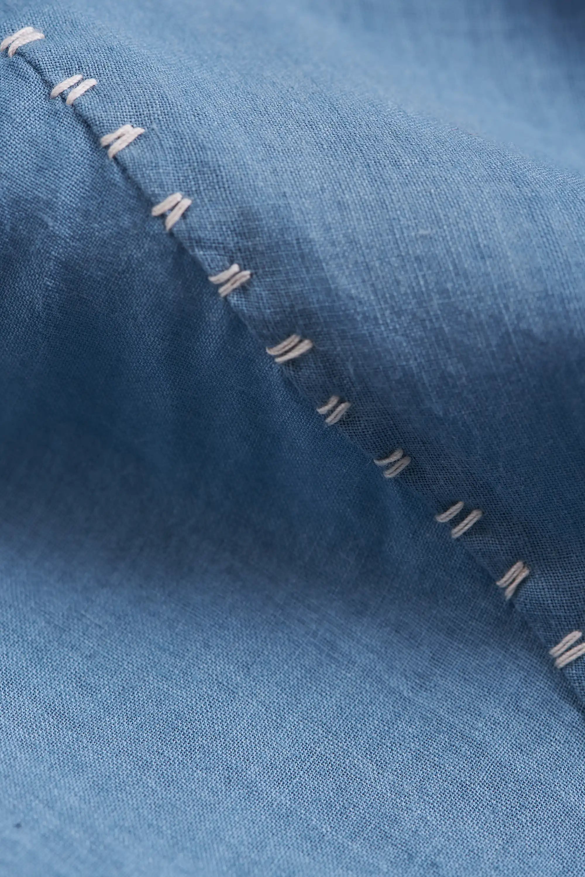 Close-up of powder blue fabric with a diagonal row of white contrast stitching.