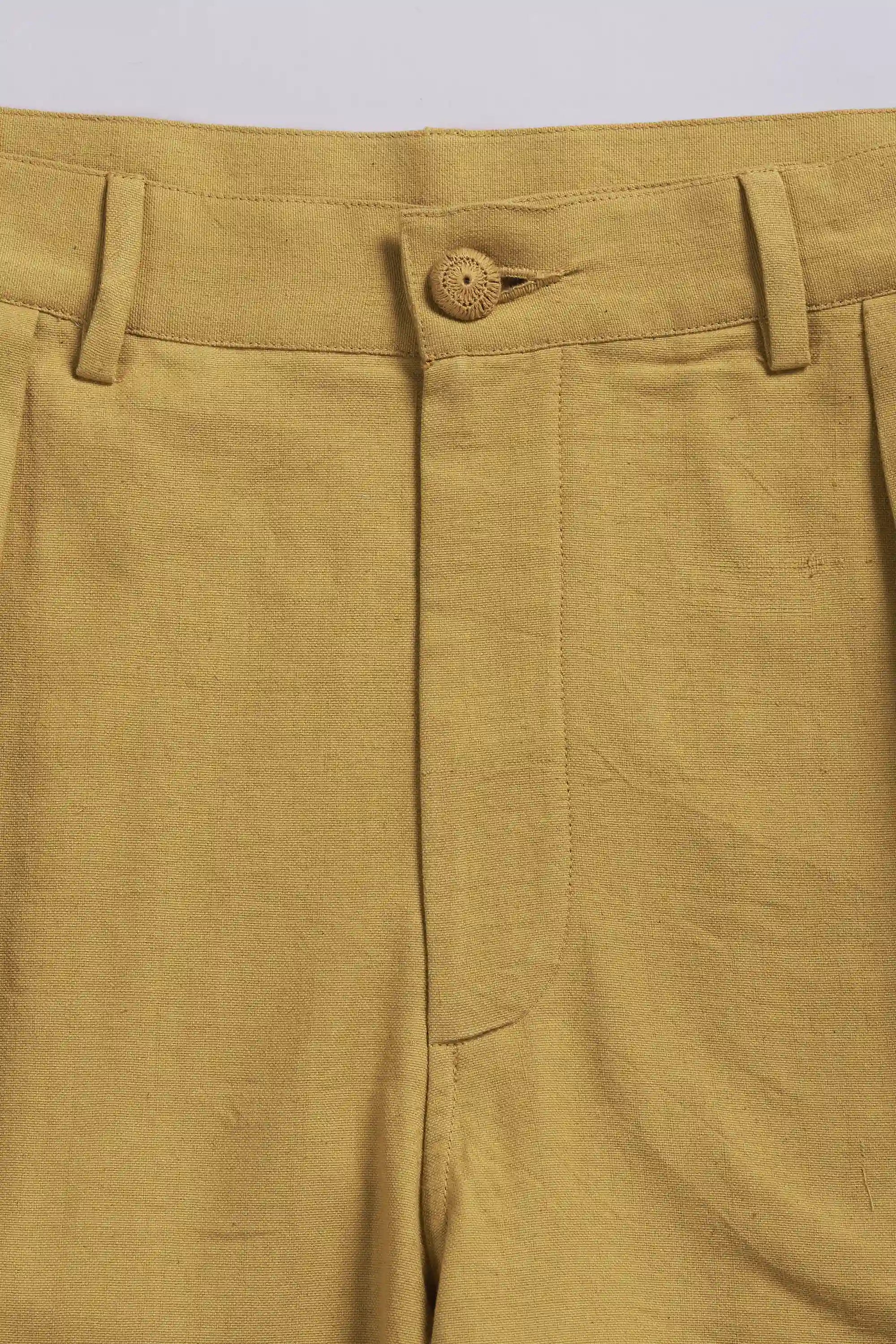 Close-up of a ochre yellow pleated pant with a button on a light grey background