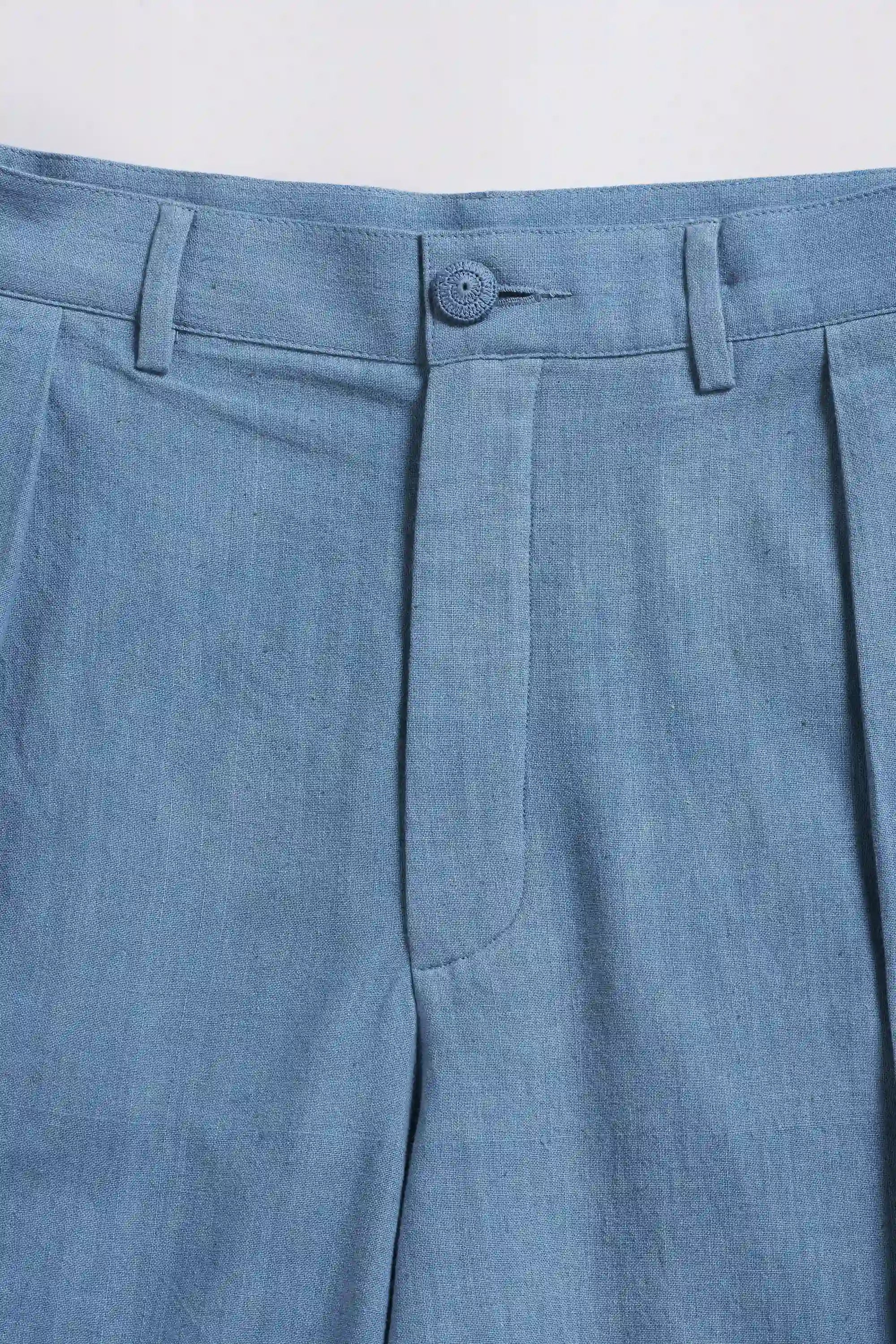 Close-up of blue pleated pants with a button on a light grey background