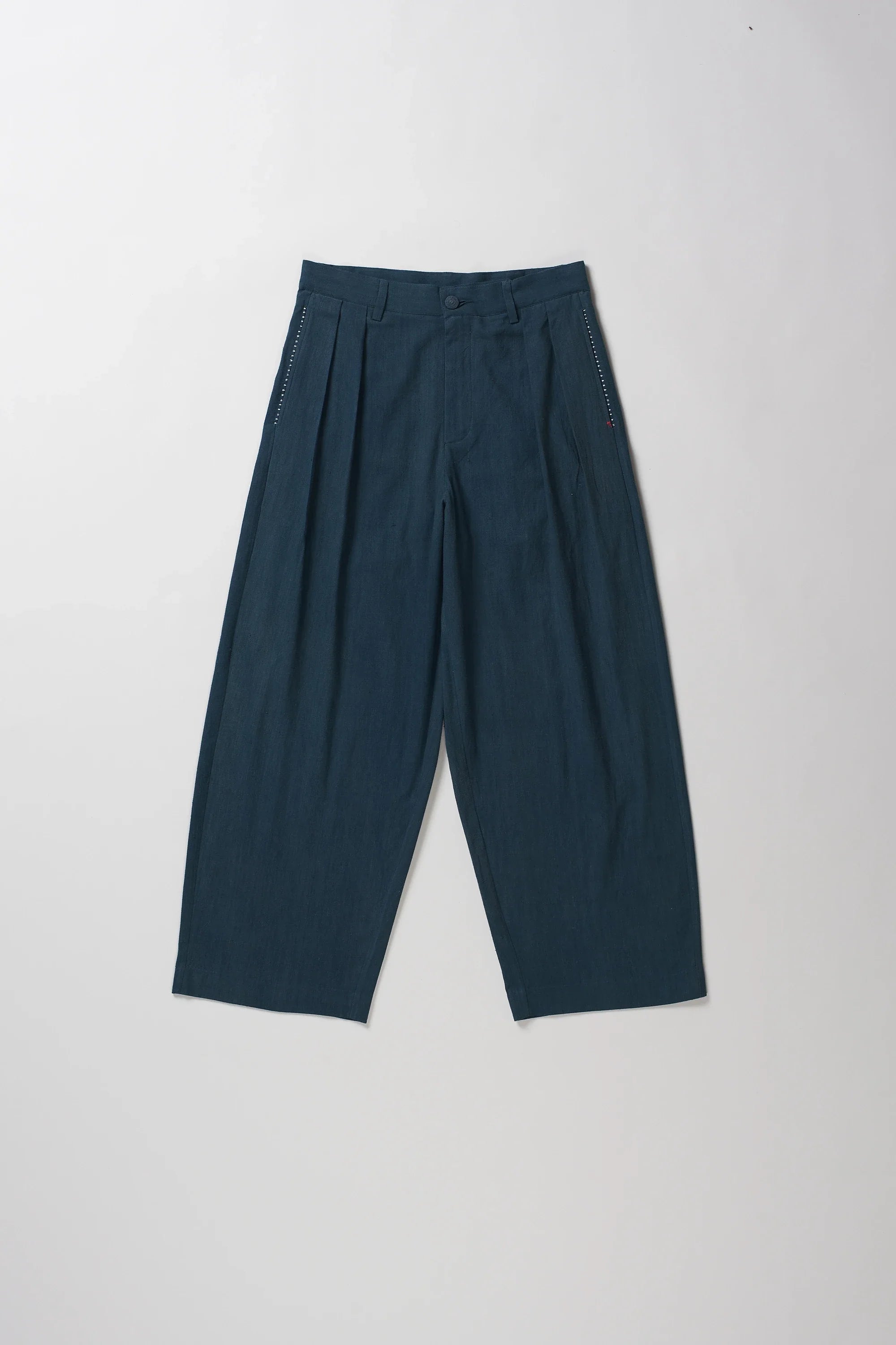 A pair of black indigo pleated trousers laid flat against a light gray background.