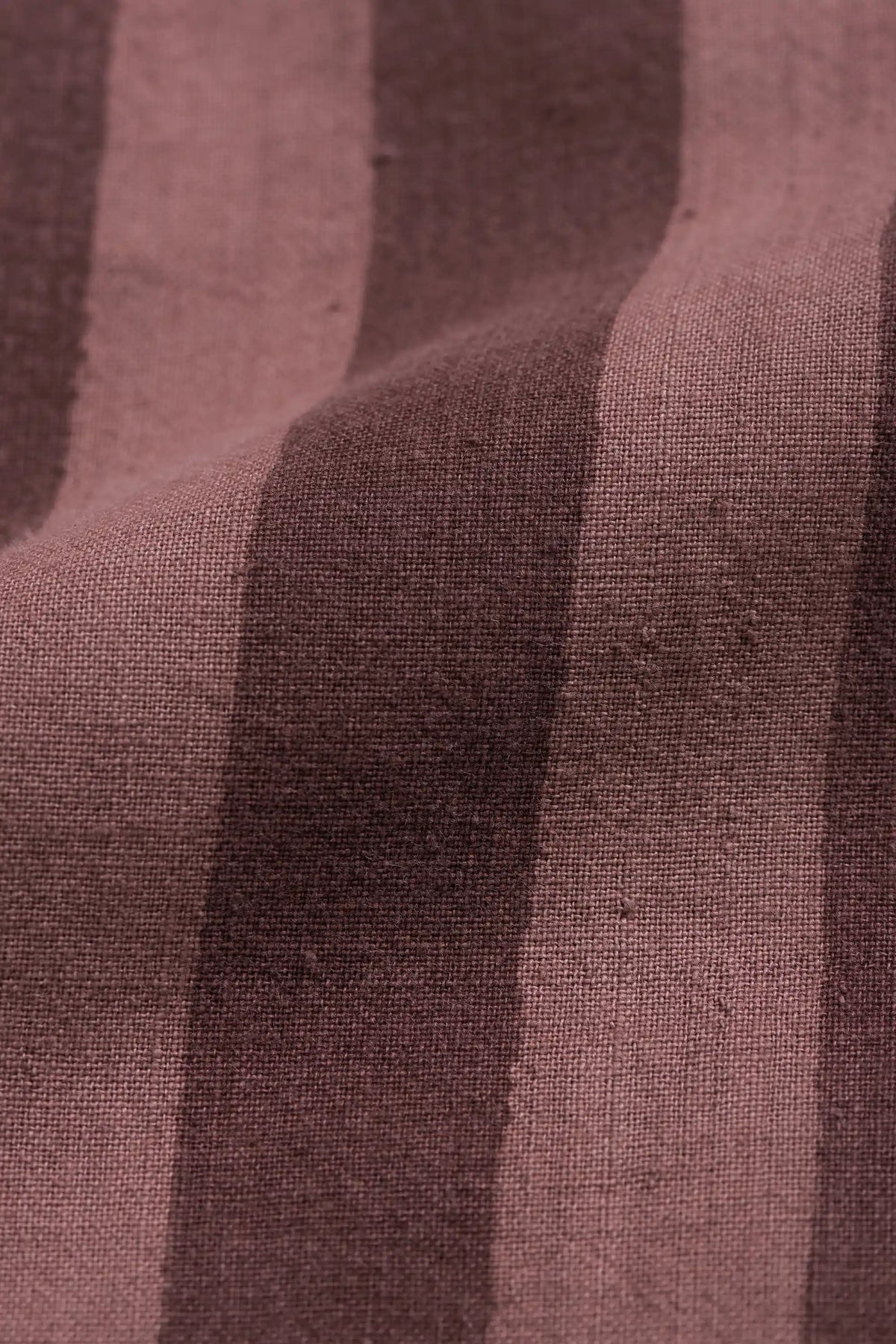 A close-up of a textured fabric with vertical stripes in dusty mauve and dark brown.