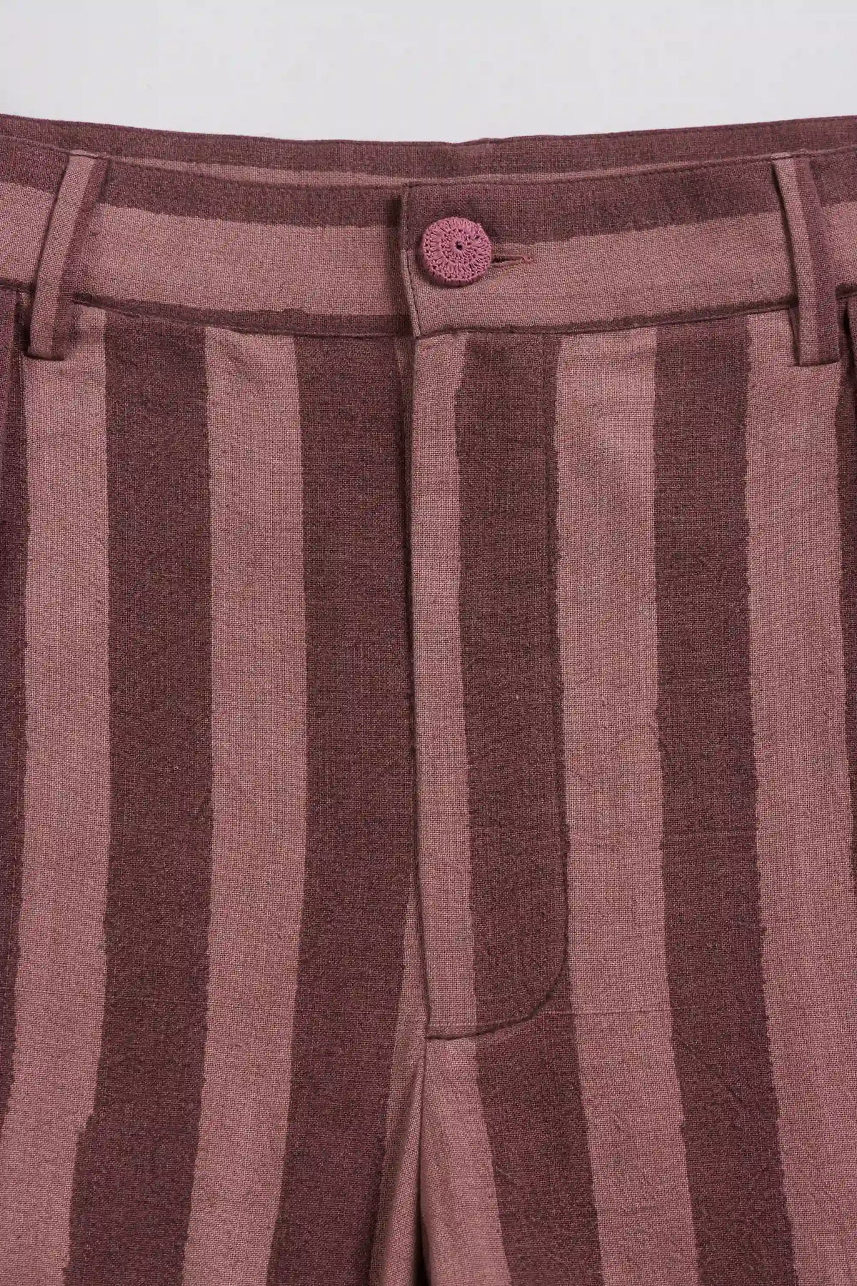 Close-up of striped trousers in dusty rose and dark brown, featuring a single button closure at the waistband.