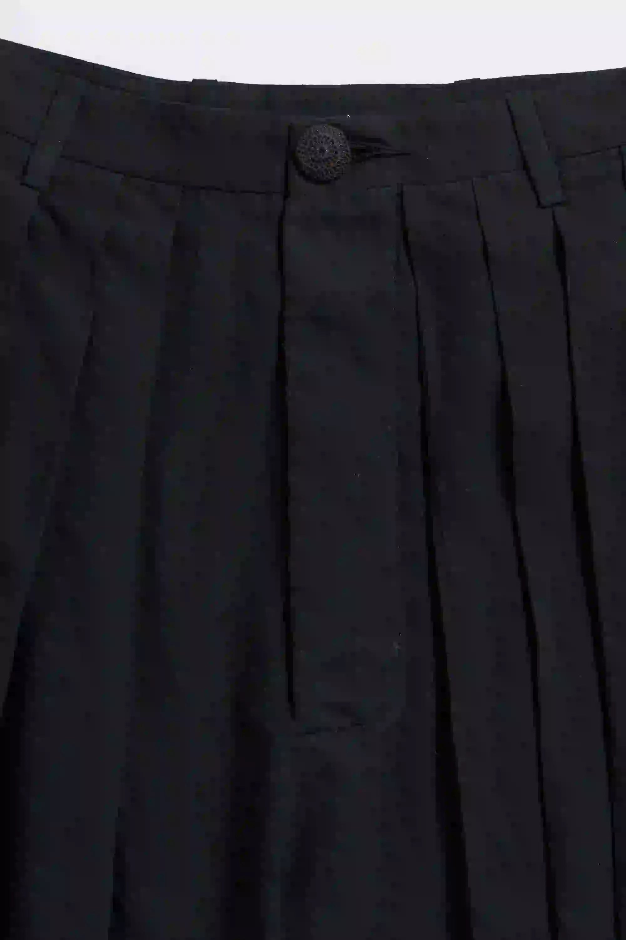 Close-up of black pleated pants with a button on a grey background
