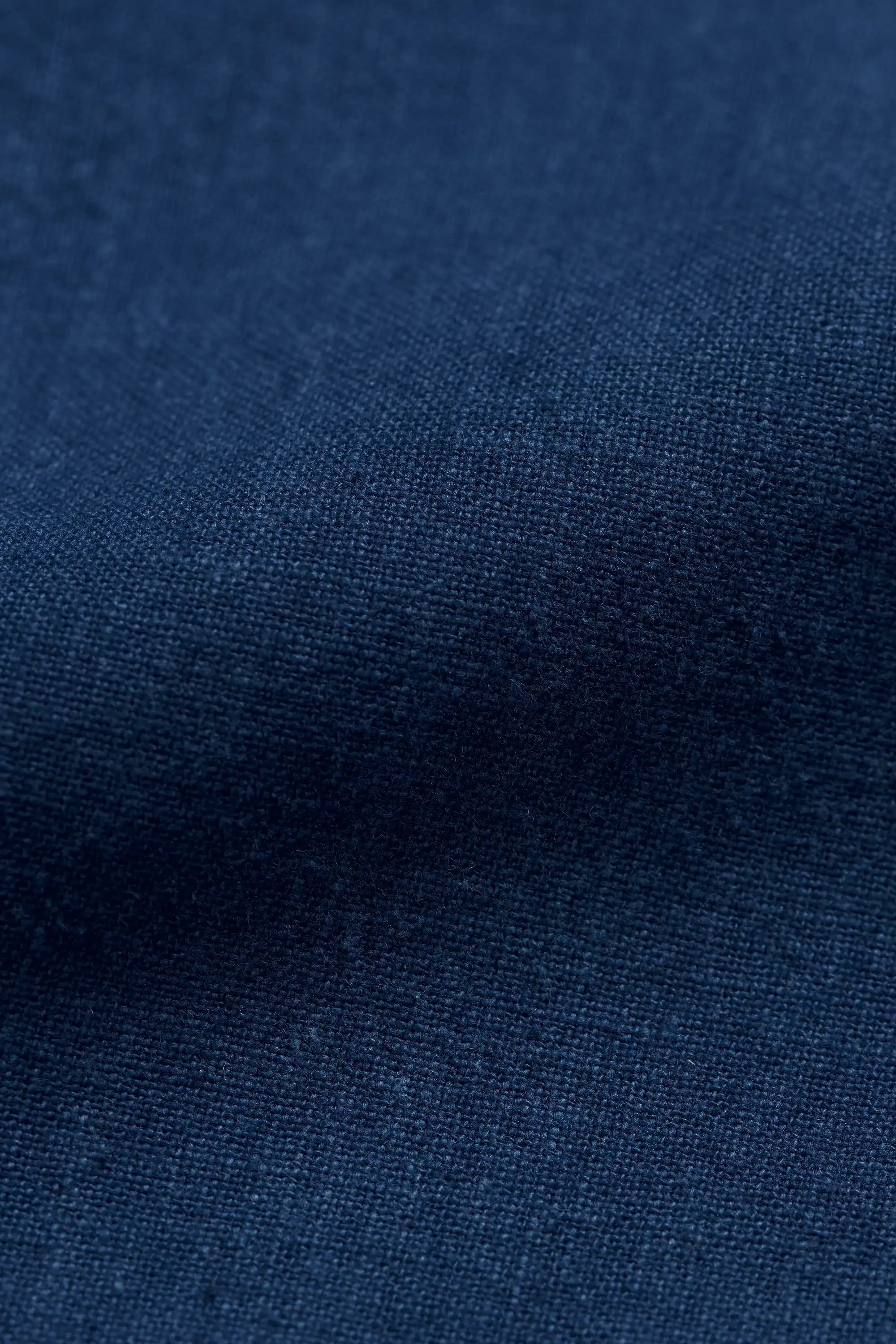 A close-up of medium indigo fabric with a visible woven texture and soft folds.