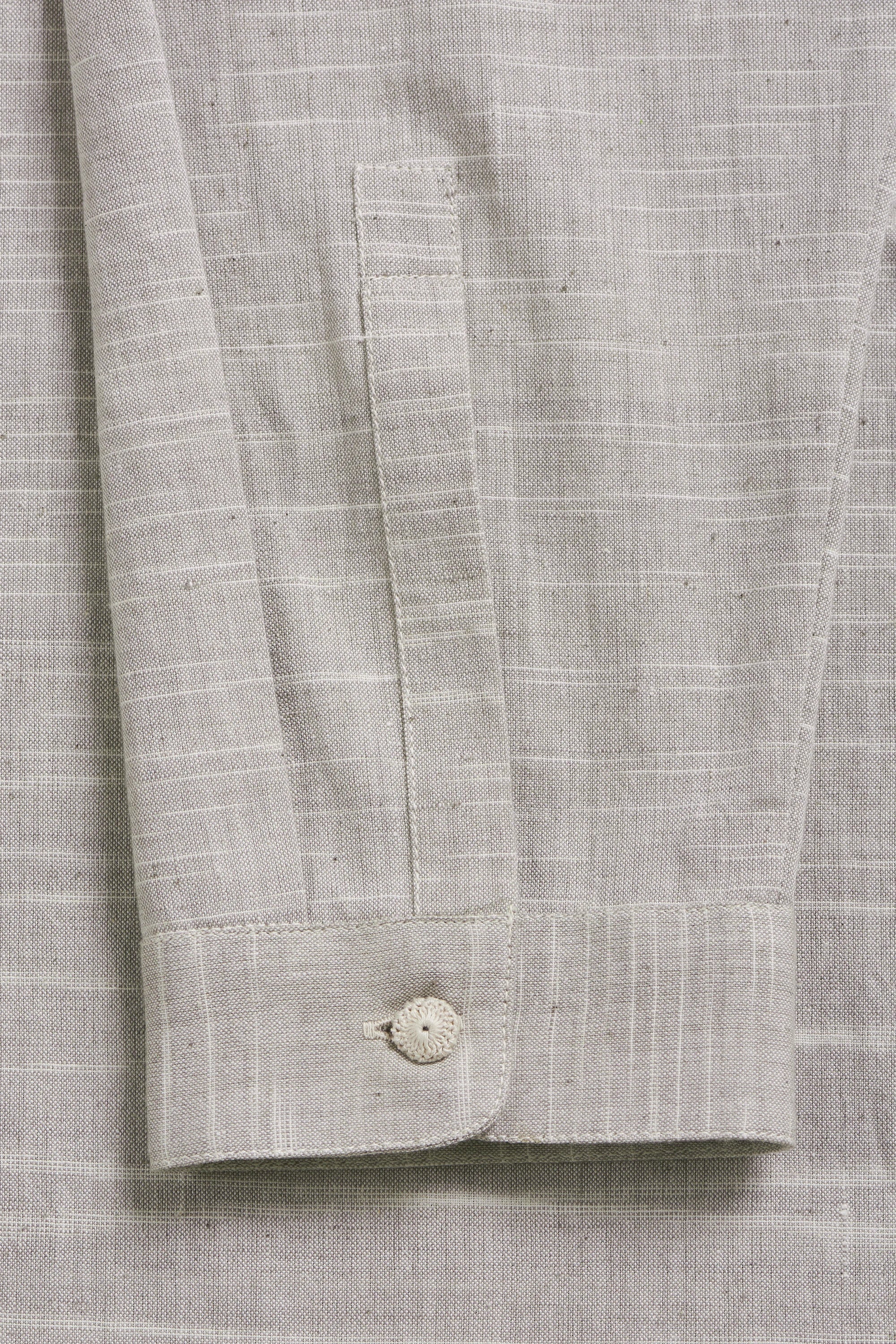 Close-up of a light gray textured shirt with a button on a matching fabric background