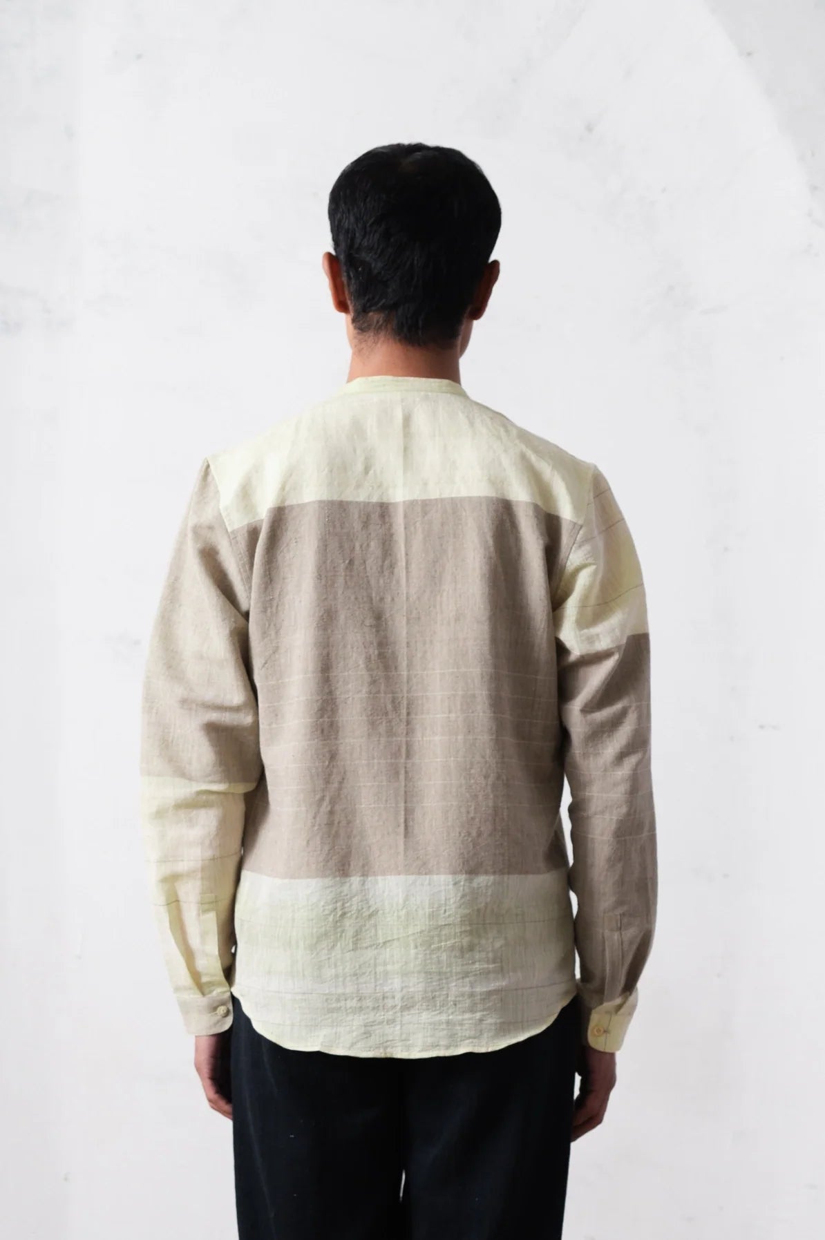 Back shot of a person wearing a beige and brown striped shirt against a light grey background
