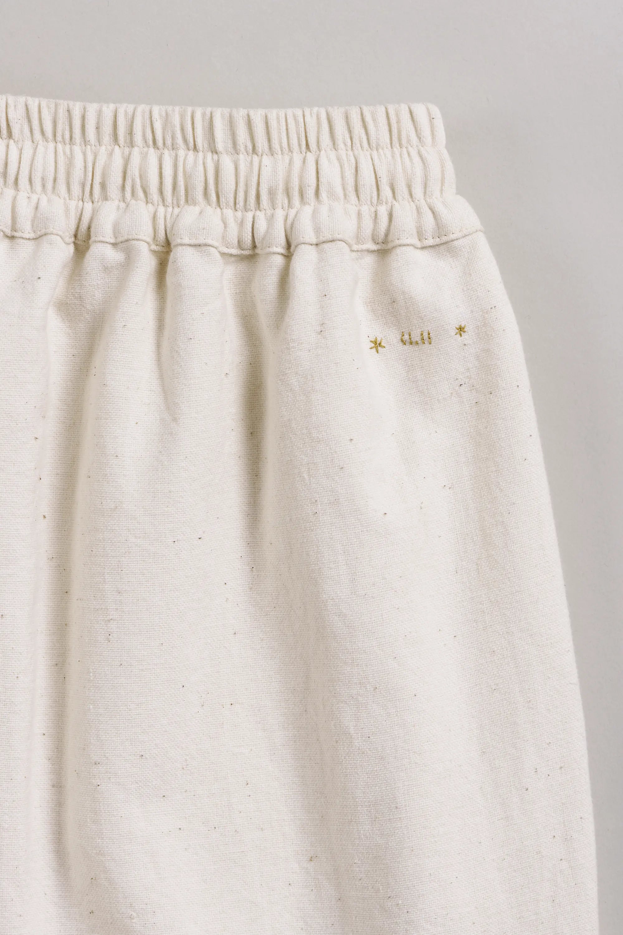 Ecru pants with a hand detailing on a grey background