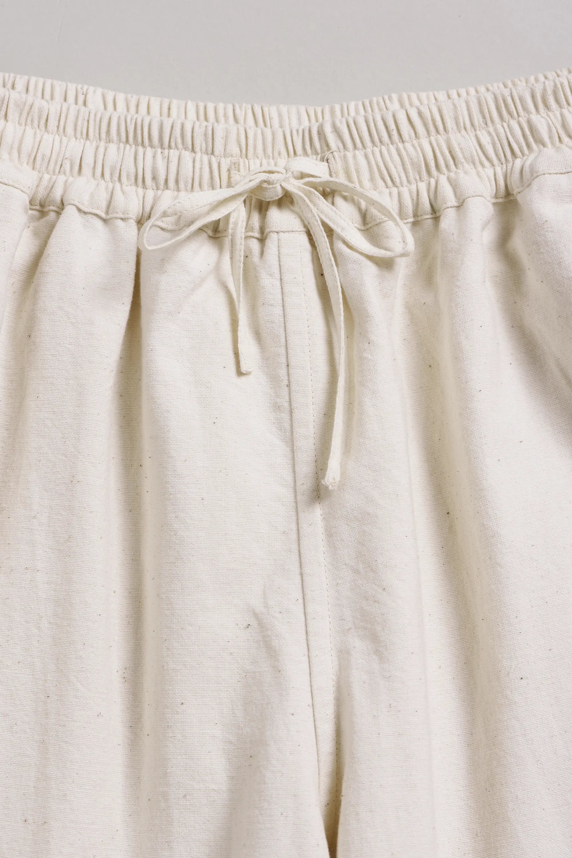 Close-up of ecru pants with a drawstring on a light grey background