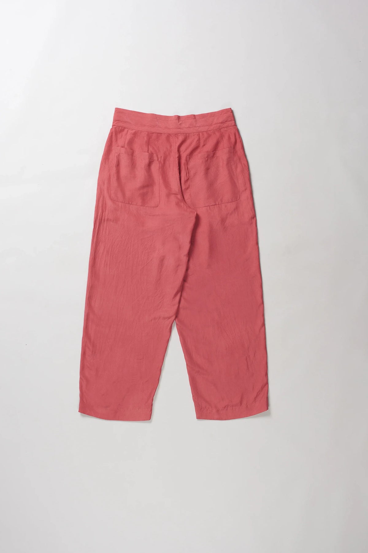 Back shot of a pair of loose-fitting, dusty rose cropped pants laid flat against a light grey background.