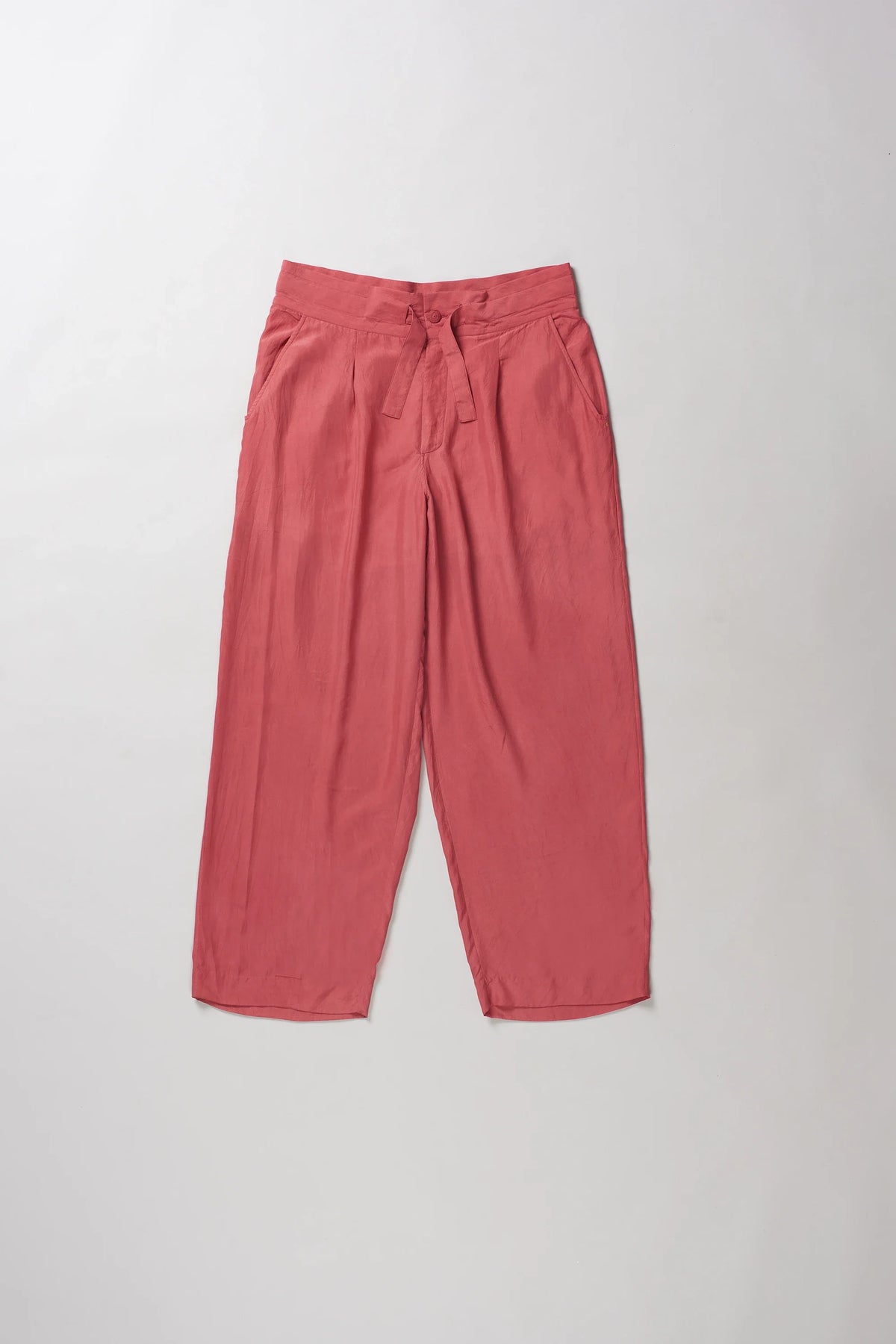 A pair of relaxed-fit, wide-leg pants in a dusty rose or muted coral pink color, laid flat against a light grey background.