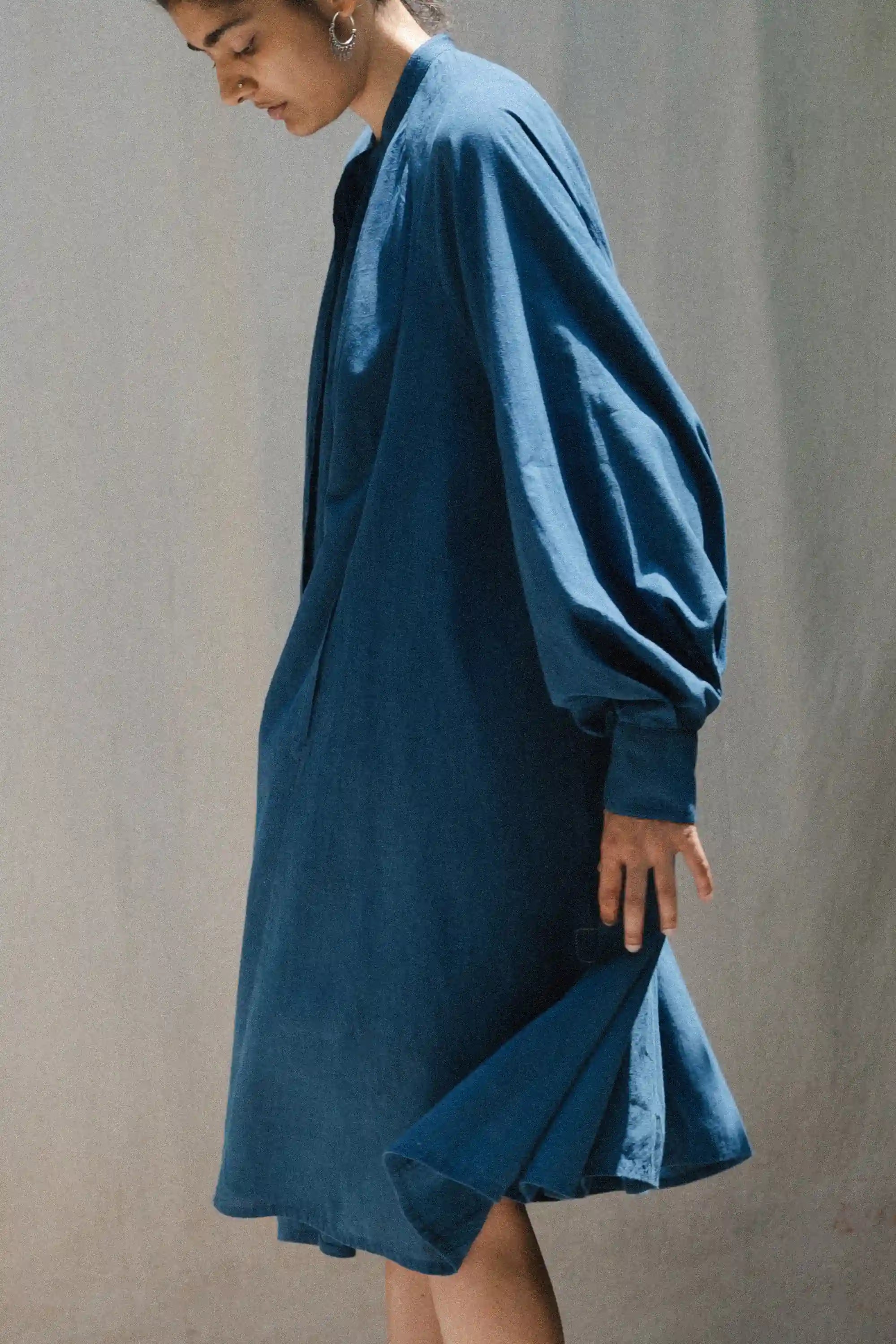 A side shot of a person wearing a blue dress against a plain background
