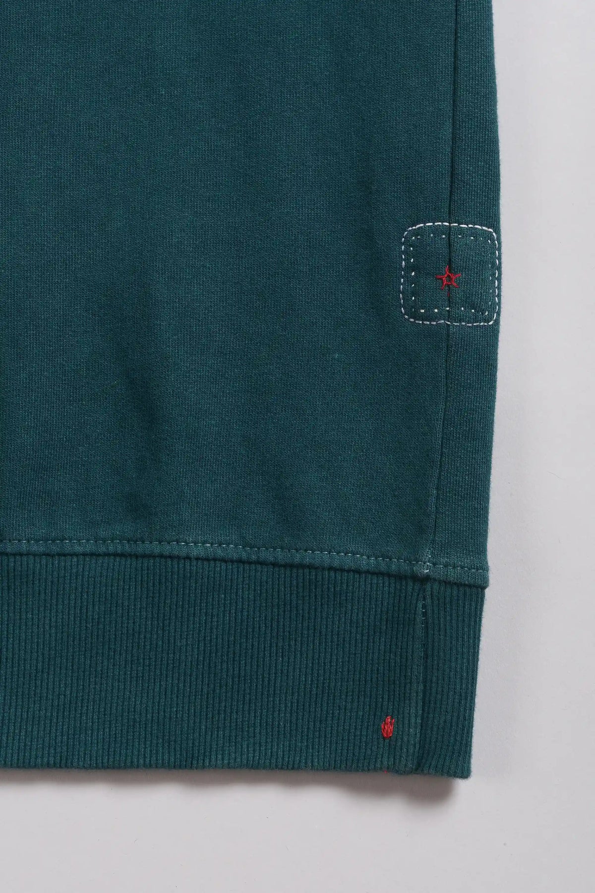 Close-up of a sweatshirt showing small square patch and red embroidered star detail, on a light grey background.