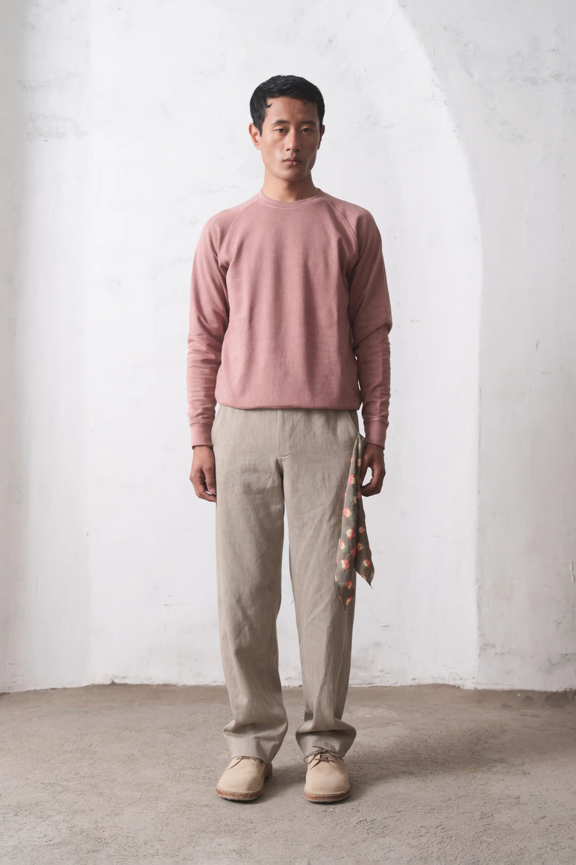 Man wearing a sweater and pants standing against a light grey wall