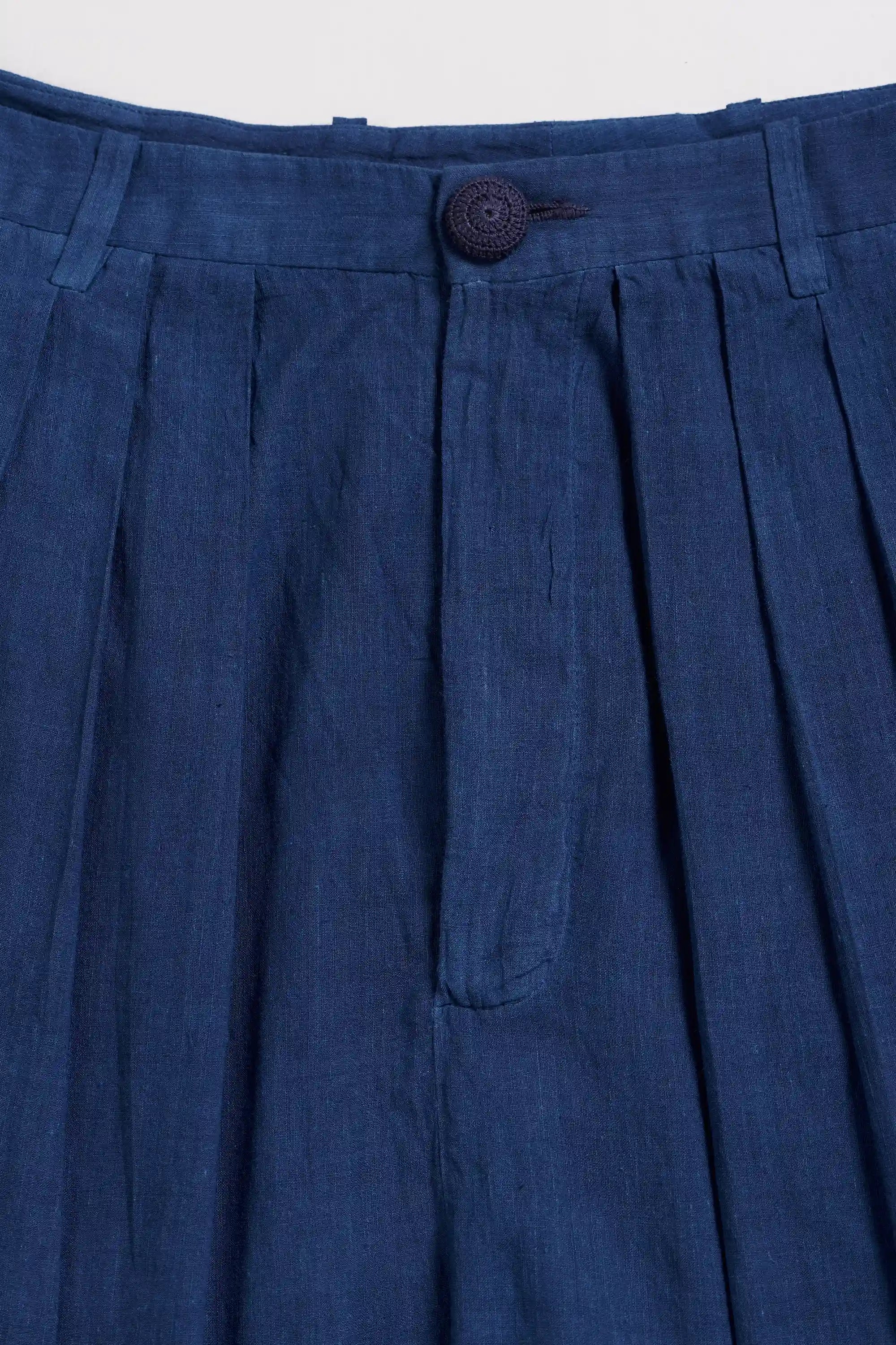 Close-up of blue pleated pant with a button on a light grey background