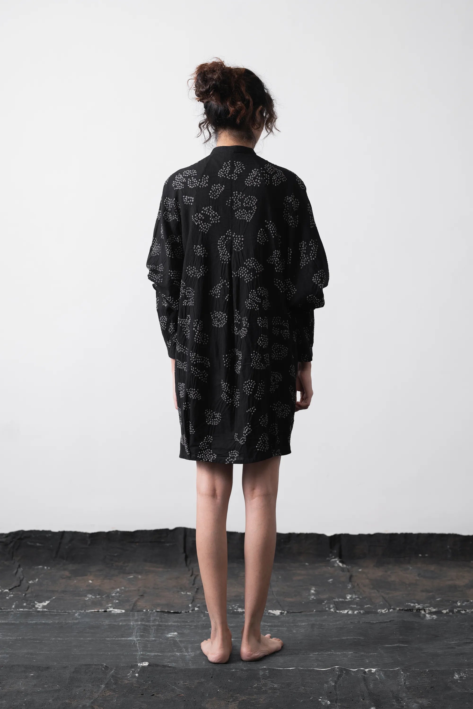 A person standing with their back to the camera wearing a black long-sleeve shirt dress.