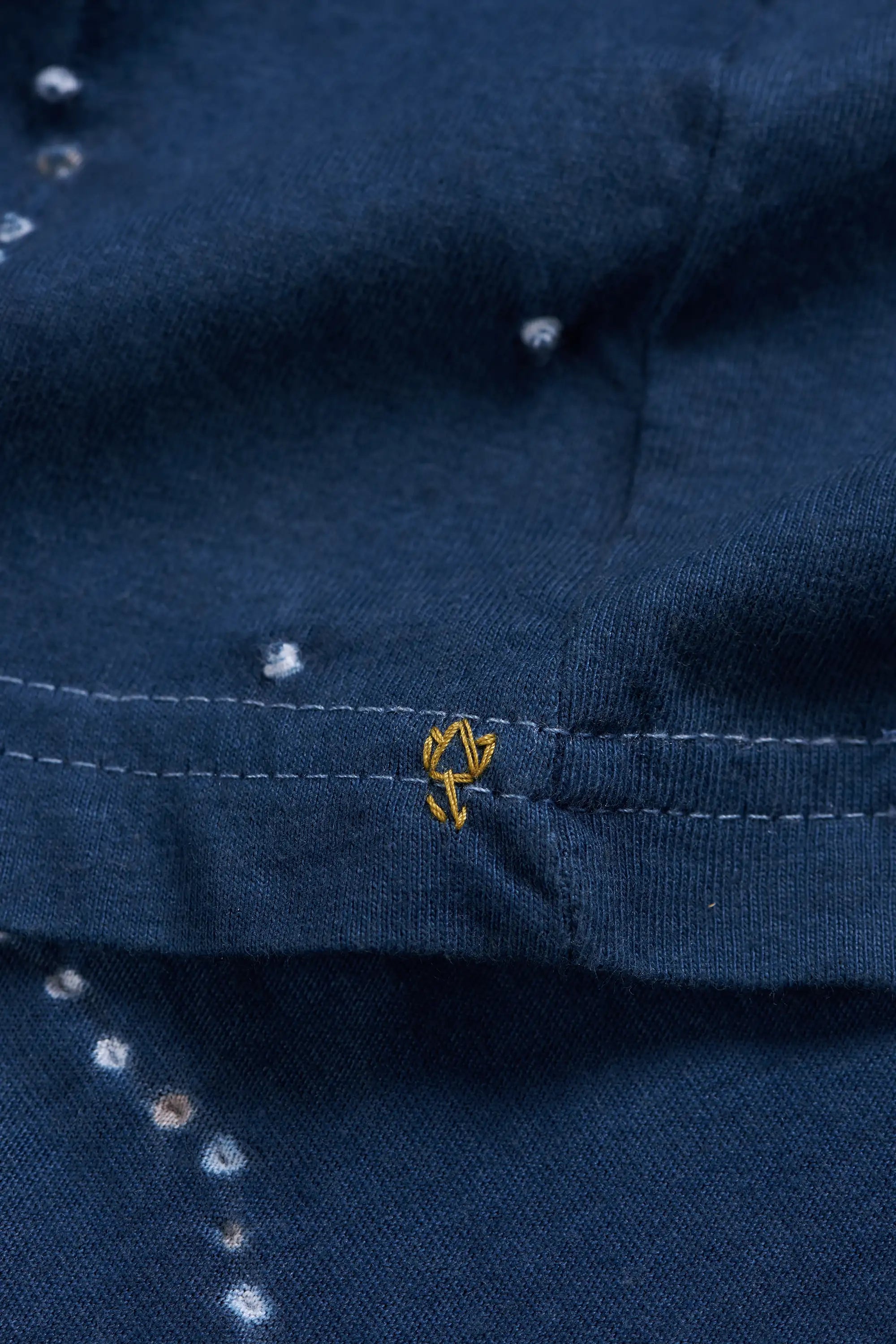 Close-up of a space blue fabric garment with a small yellow embroidered details.