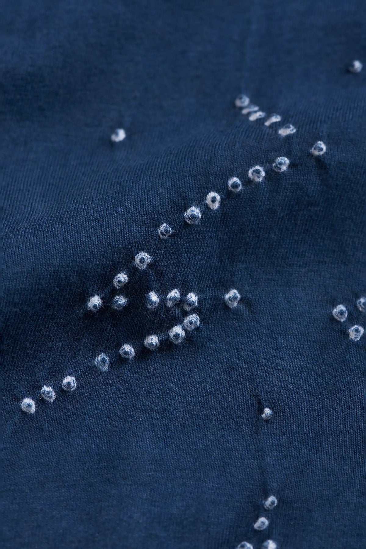 Close-up of a space blue fabric surface decorated with scattered small clear bandhani pattern.
