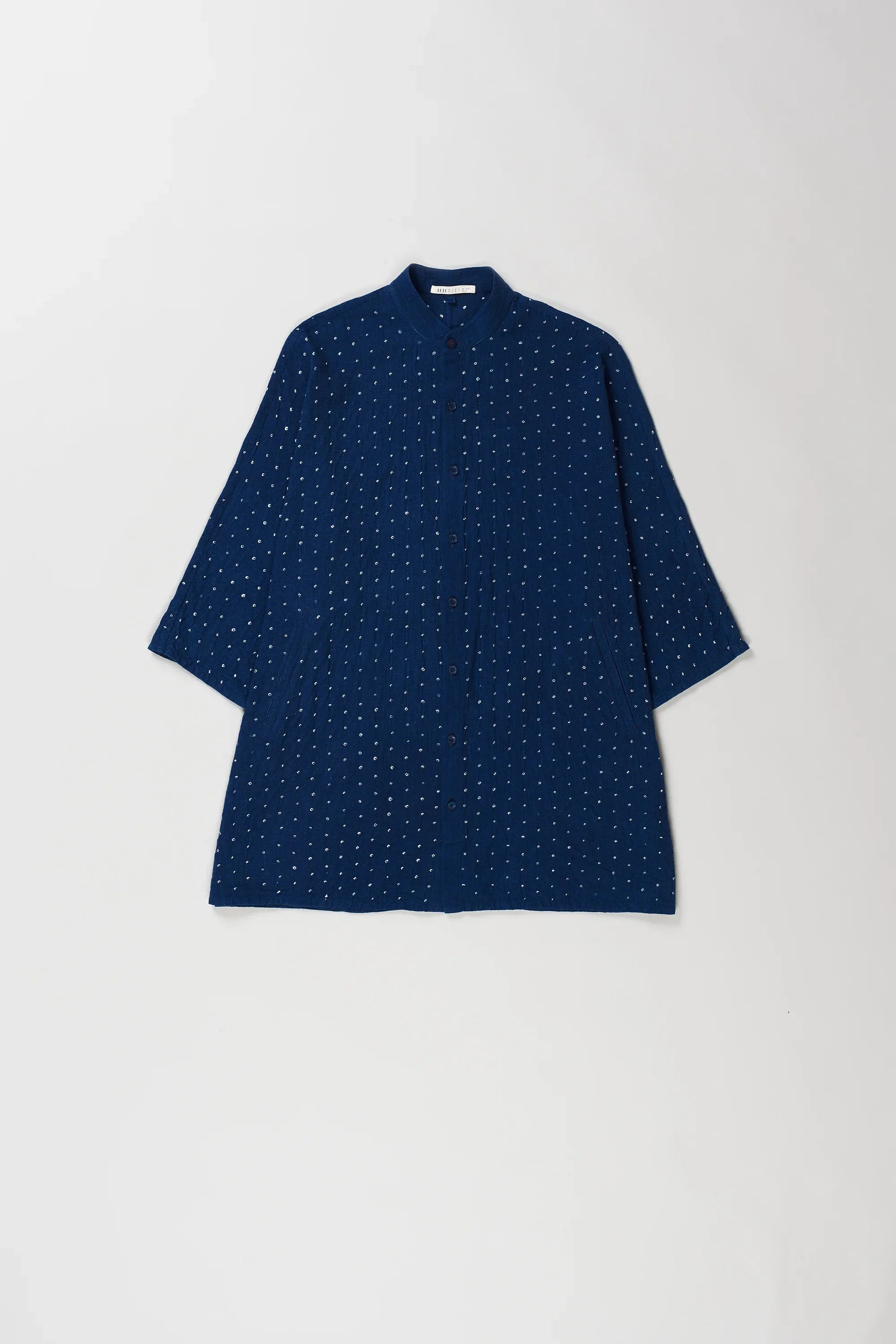 A medium indigo short-sleeve shirt with a bandhani dot pattern, laid flat against a light gray background.