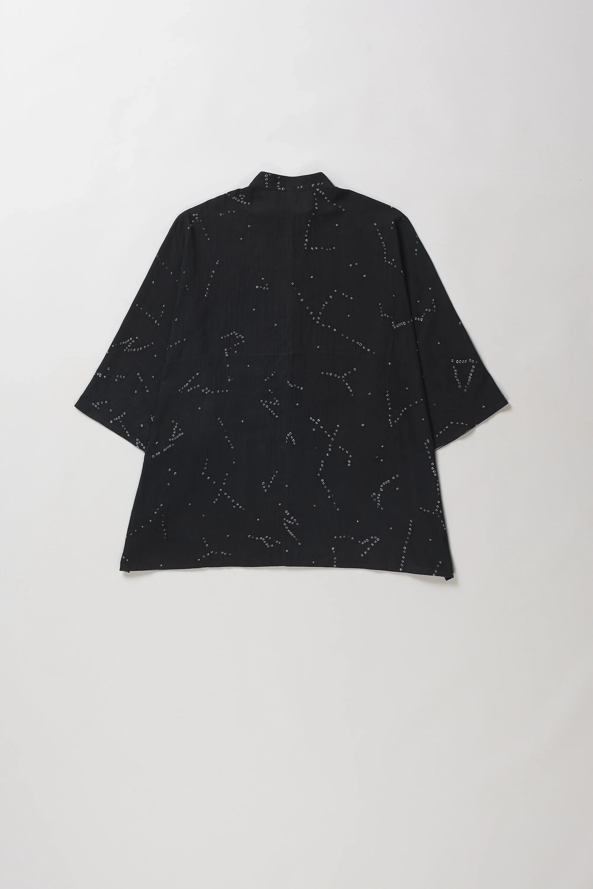 Back shot of black short-sleeve button-up shirt with an all-over white line-art constellation pattern bandhani, laid flat against a light grey background.