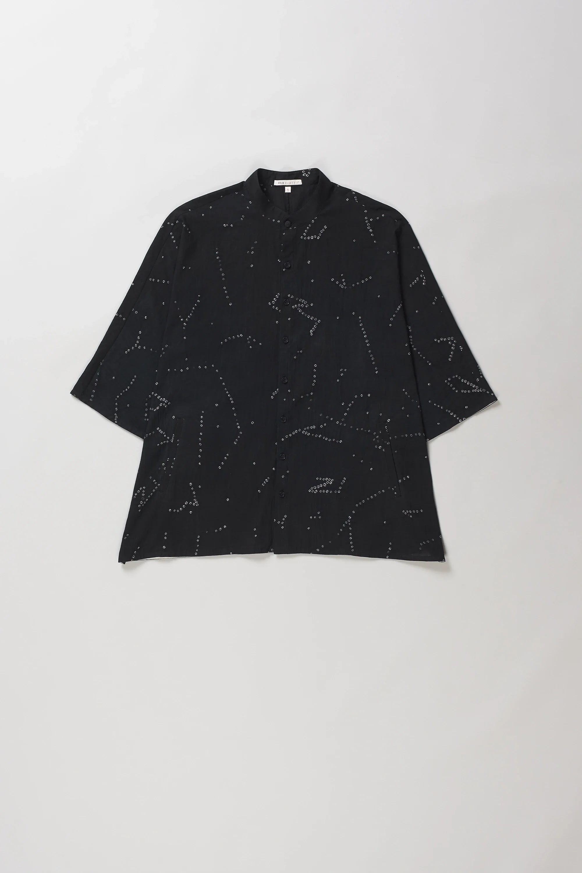 A black short-sleeve button-up shirt with an all-over white line-art constellation pattern bandhani, laid flat against a light grey background.