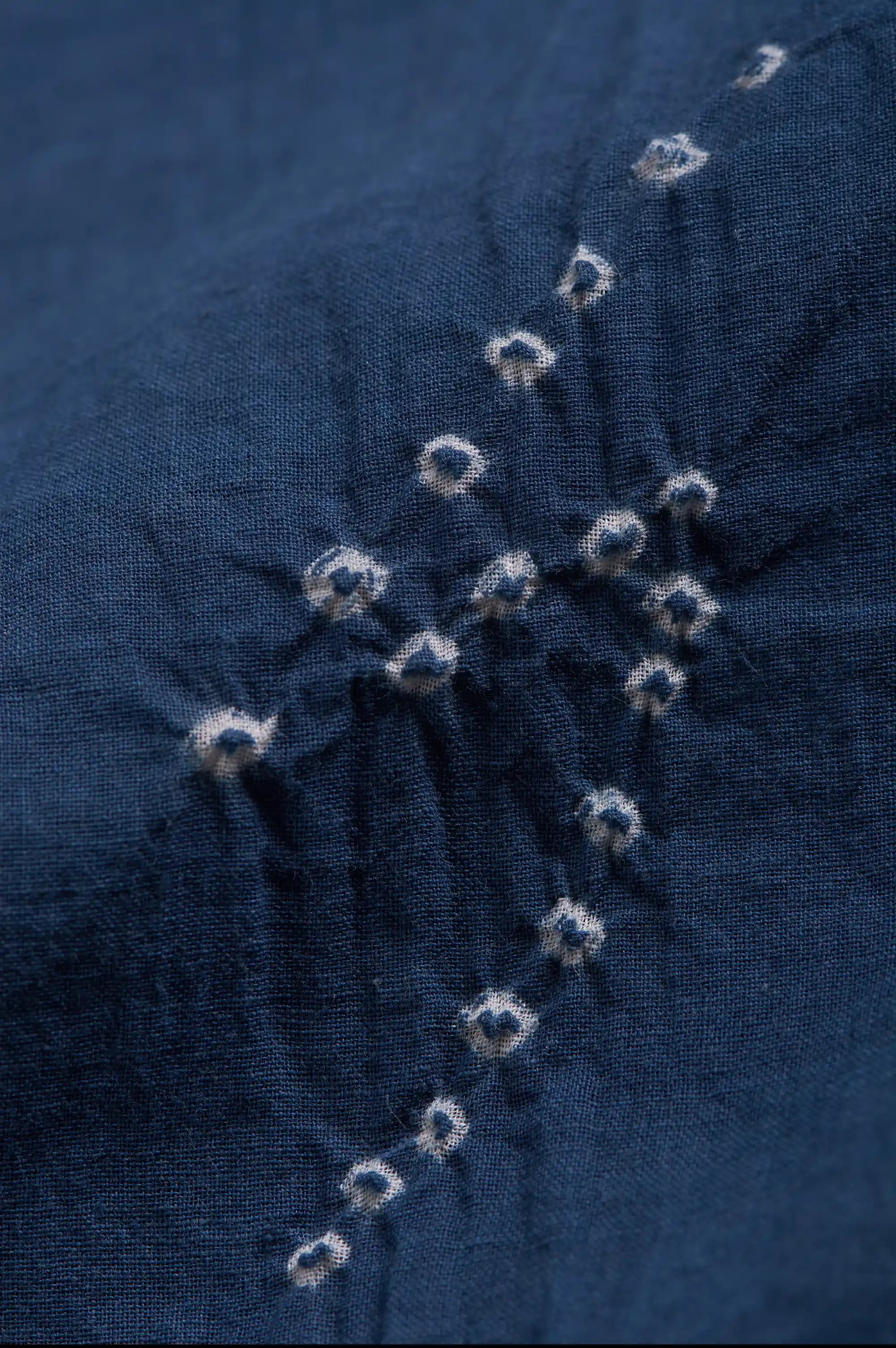 Close-up of space blue fabric with a diagonal line of white tie-dye shibori knot patterns.