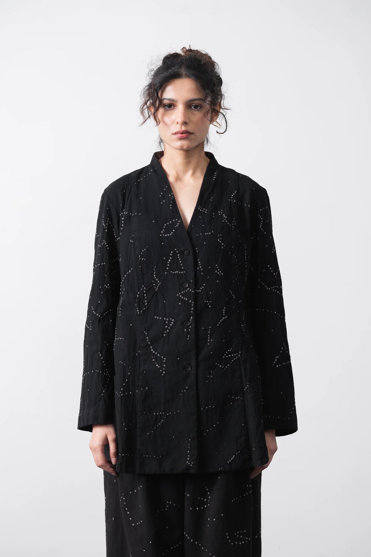 A model wearing a black long-sleeve kimono-style shirt with white dotted star patterns, paired with matching black pants, against a plain light grey background.