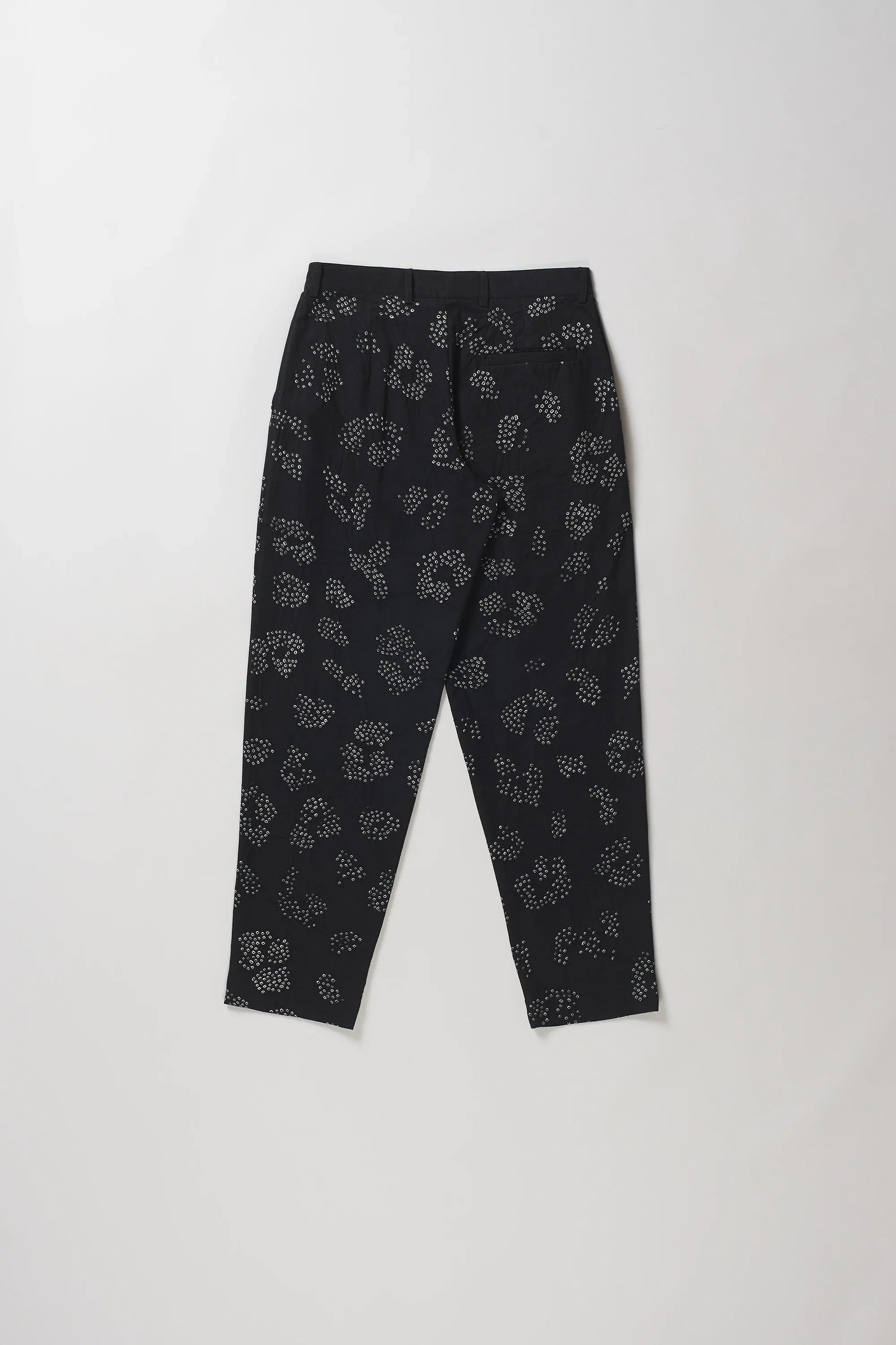 Back shot of black trousers with a white floral bandhani, laid flat against a light grey background.