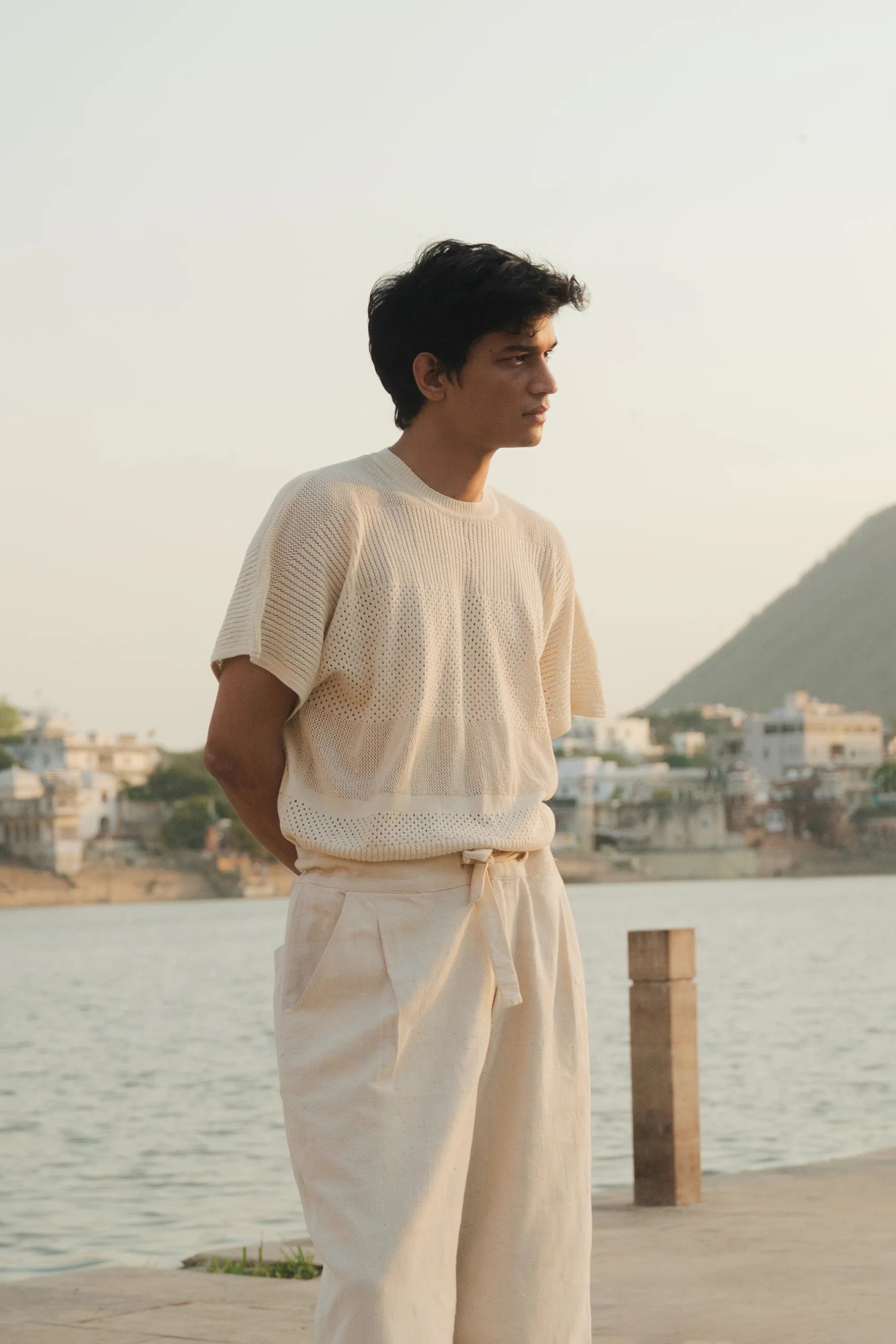 Man in ecru outfit standing by a waterfront with a scenic background