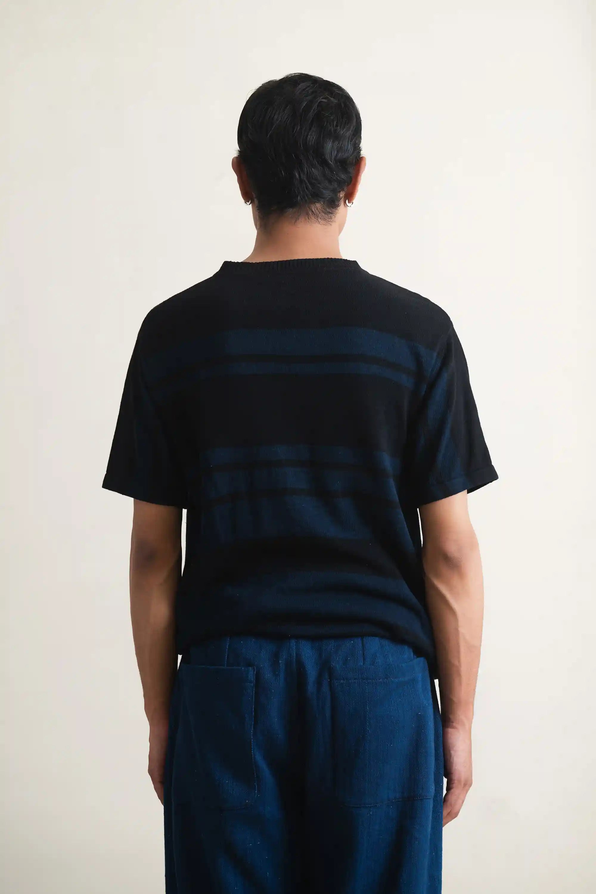 Person wearing a black t-shirt with blue stripes from behind on a white background